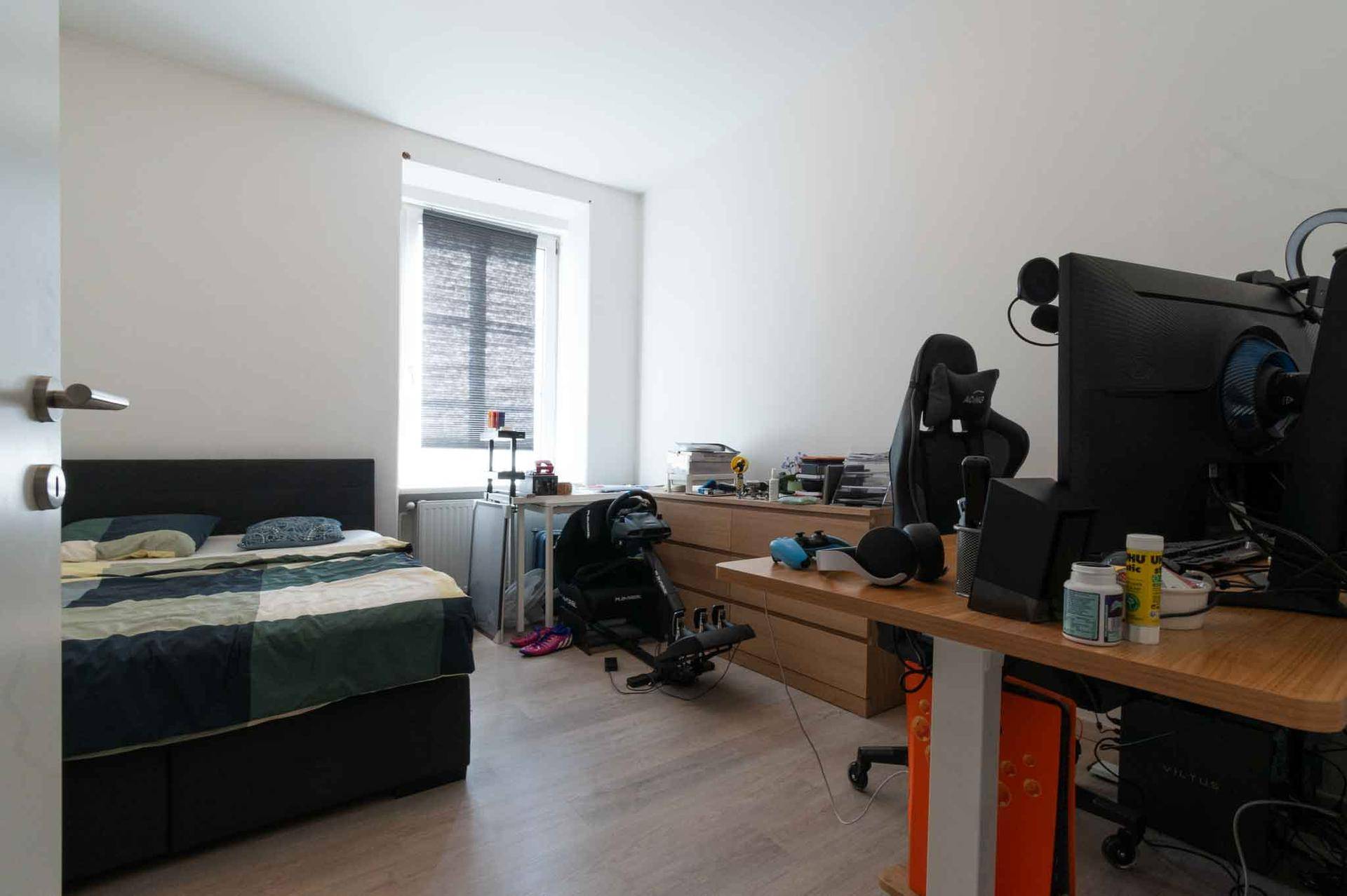 Schlafzimmer mit Bett, Schreibtisch und Gaming-Setup, ideal für Arbeit und Freizeit.