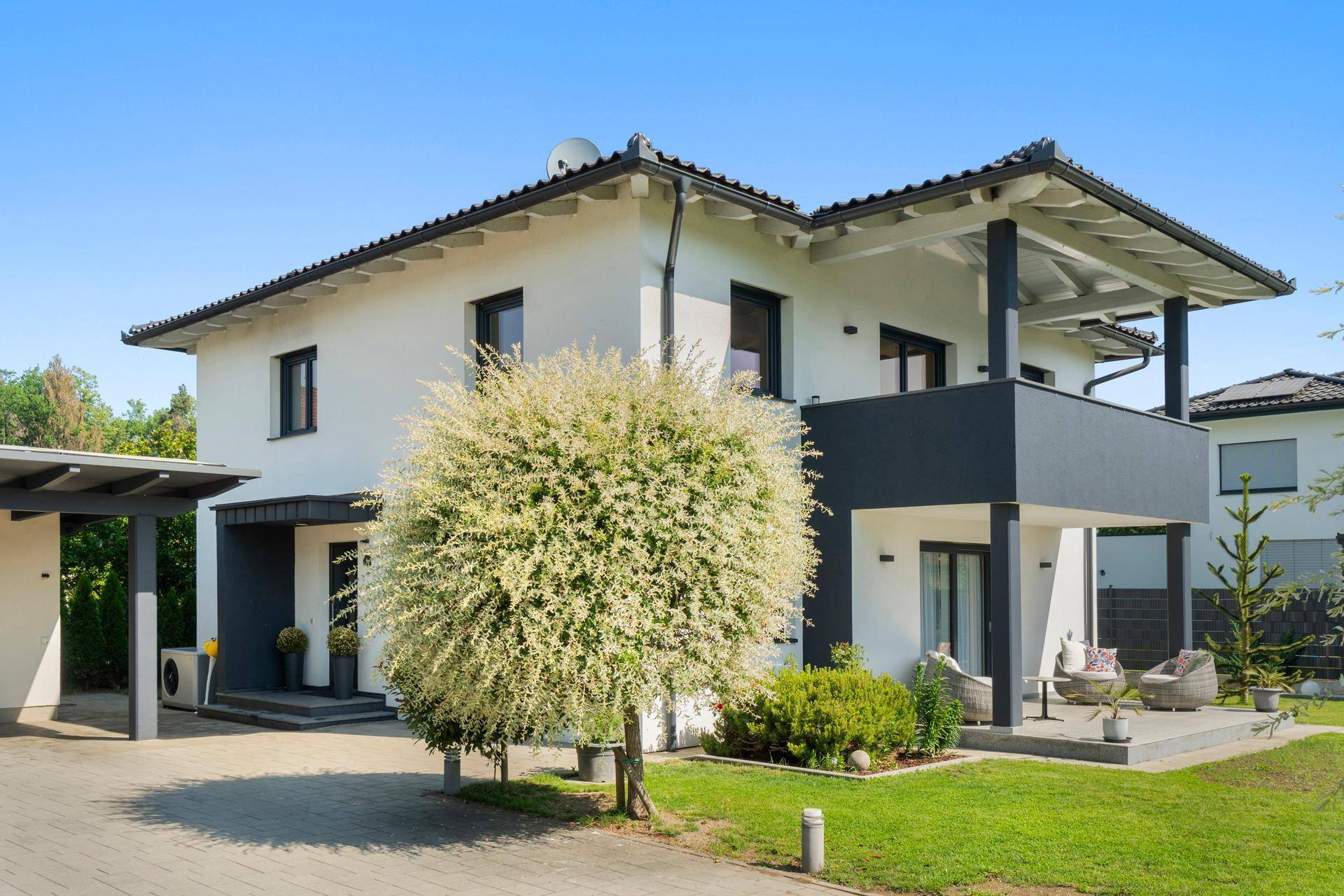 Seitenansicht des modernen Hauses mit Balkon und gemütlicher Terrasse.