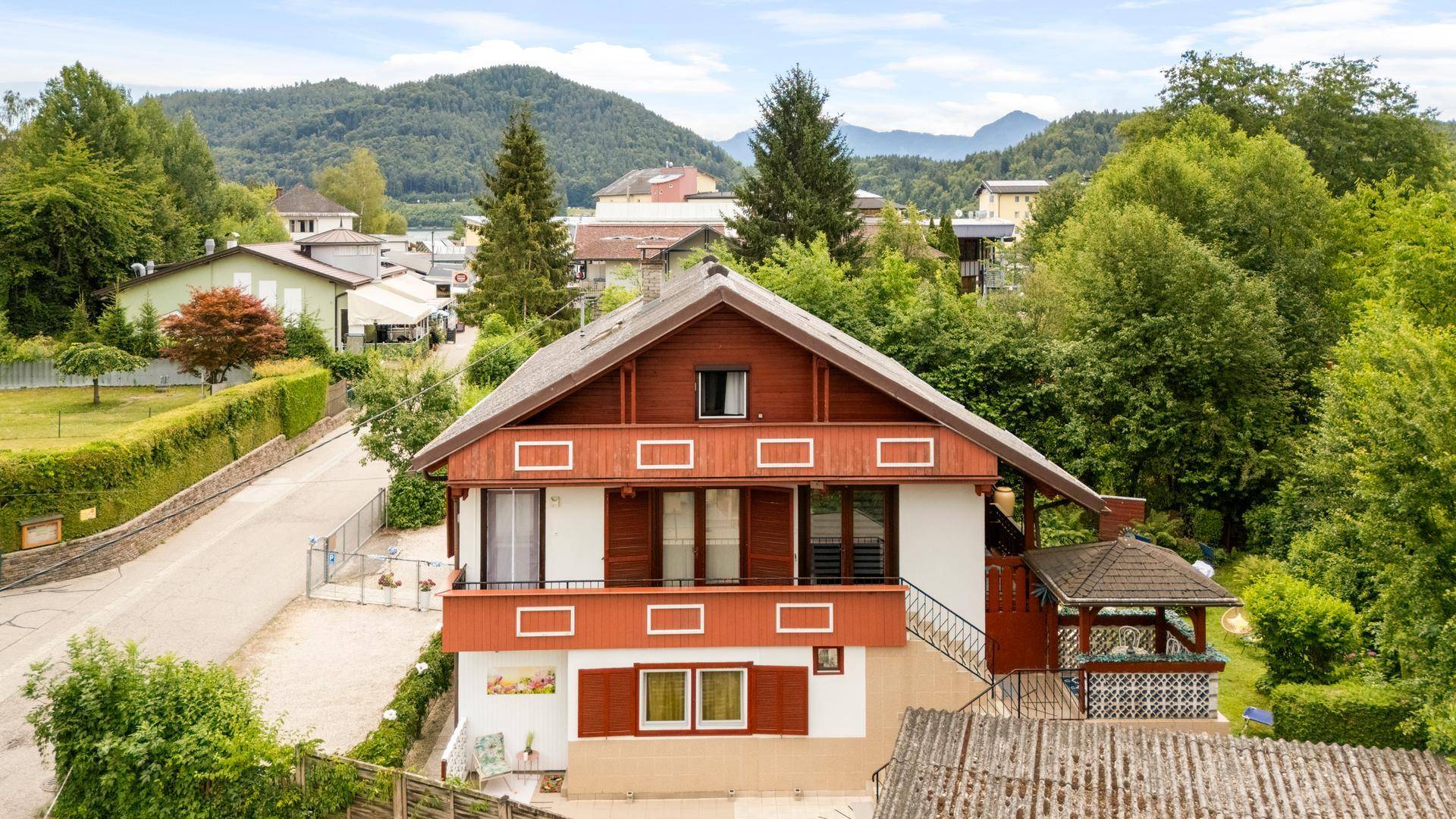 Traditionelles Haus mit Holzverkleidung, Balkonen und einem kleinen Pavillon, umgeben von viel Grün.