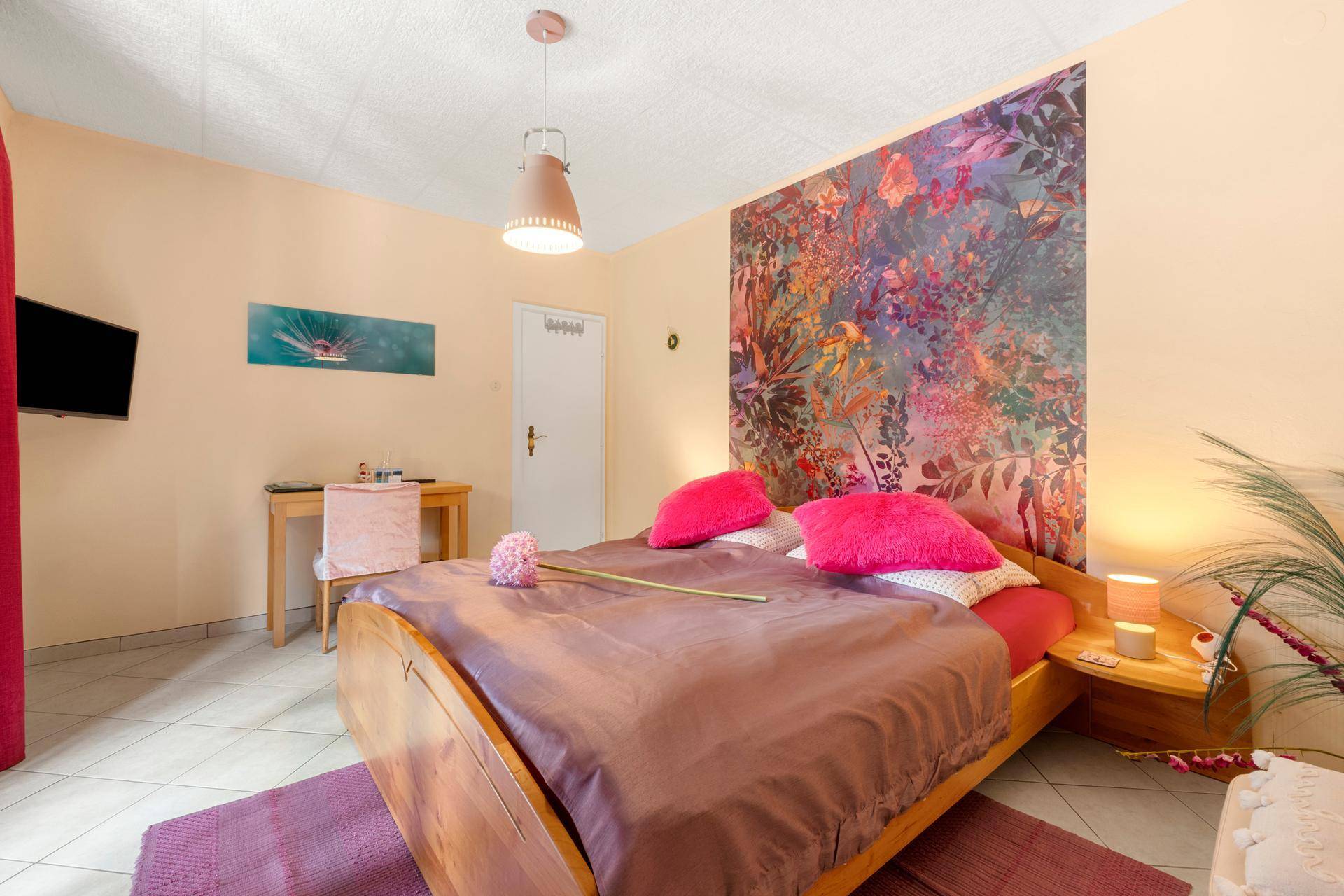 Helles Schlafzimmer mit Doppelbett, Schreibtisch und farbenfroher Blumen-Tapetenwand.