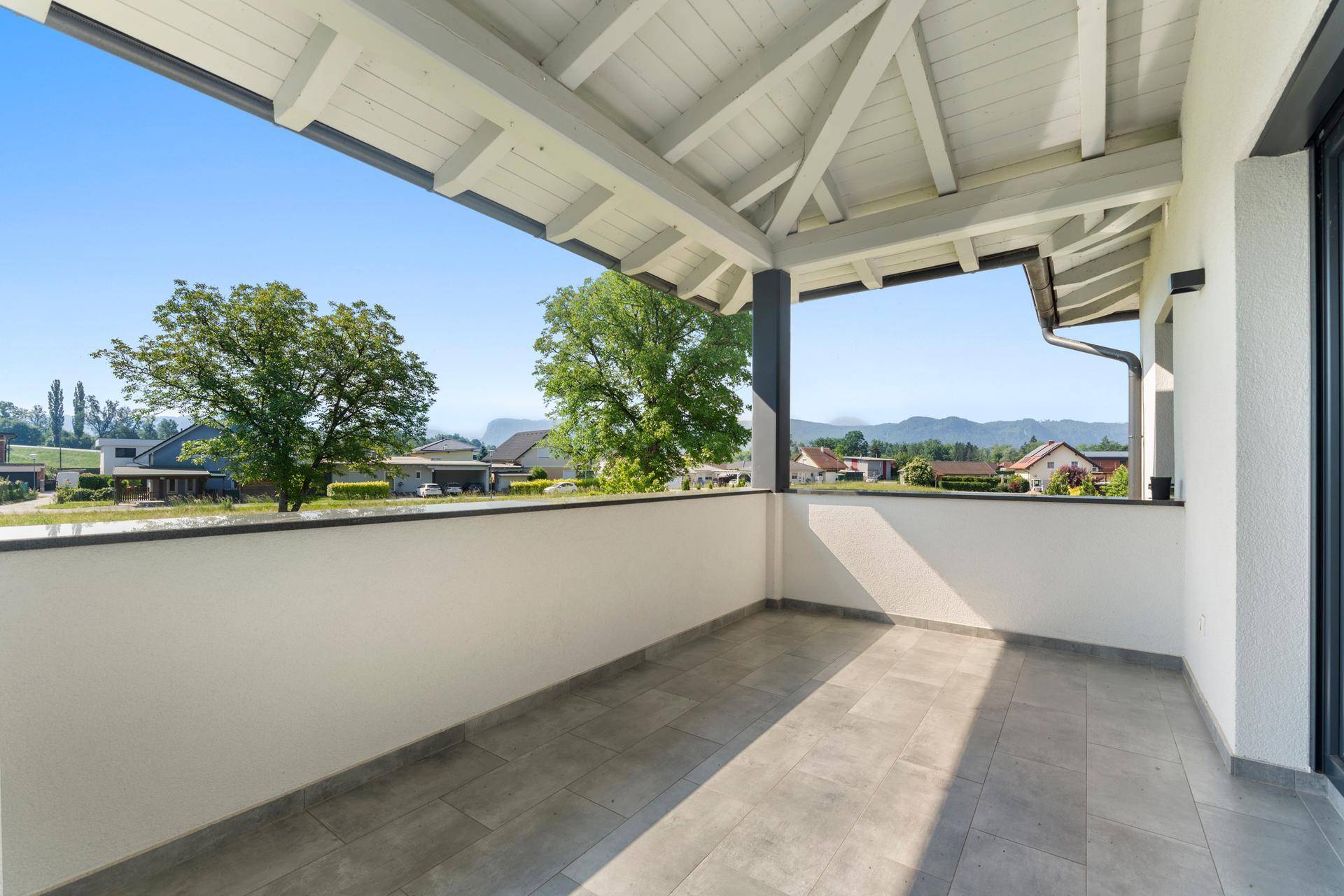 Überdachter Balkon mit Fliesenboden und weitem Blick auf die umliegende Landschaft und Berge.