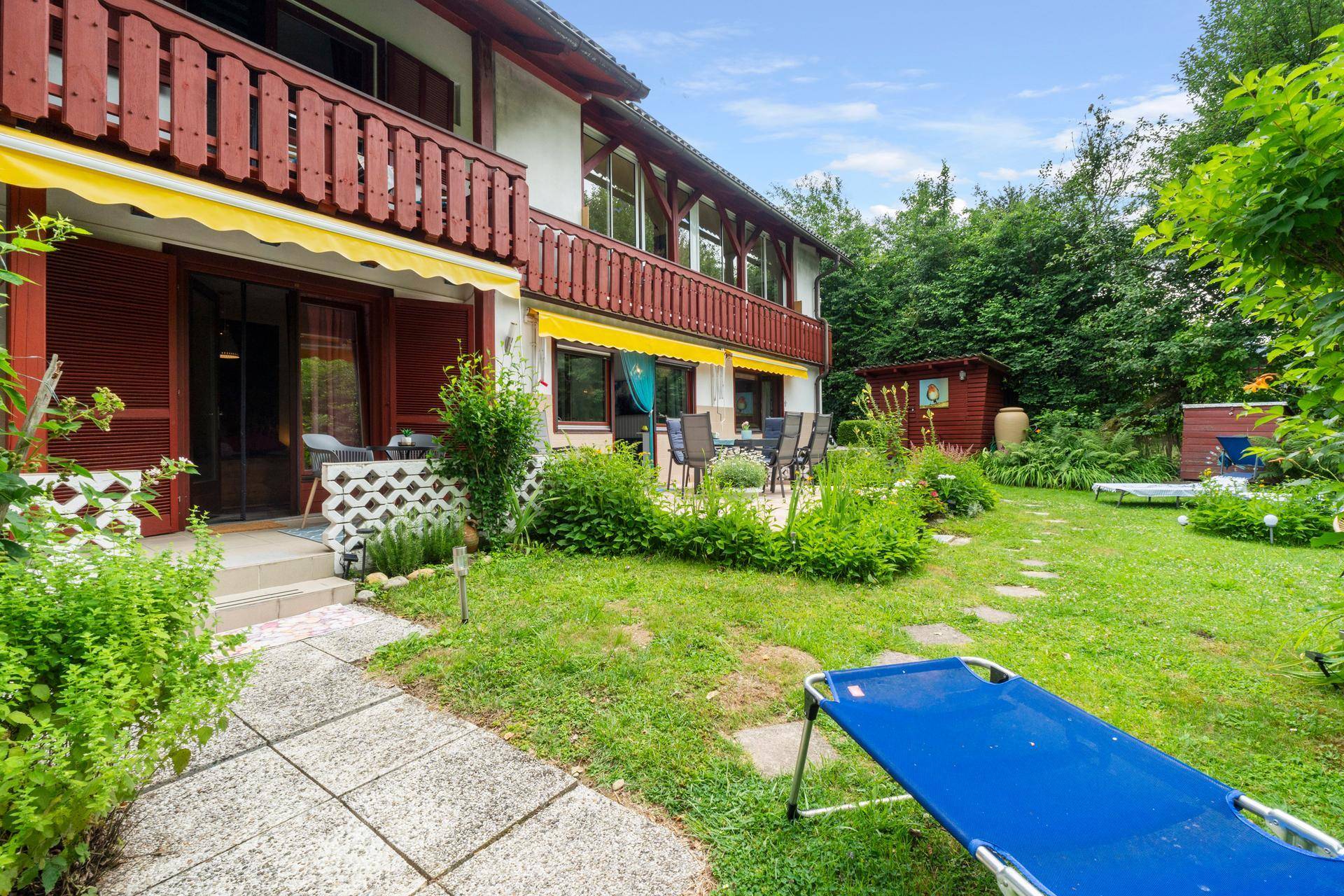 Ruhiger Gartenbereich mit Terrasse, Esstisch und Gartenhaus, umgeben von üppigem Grün.