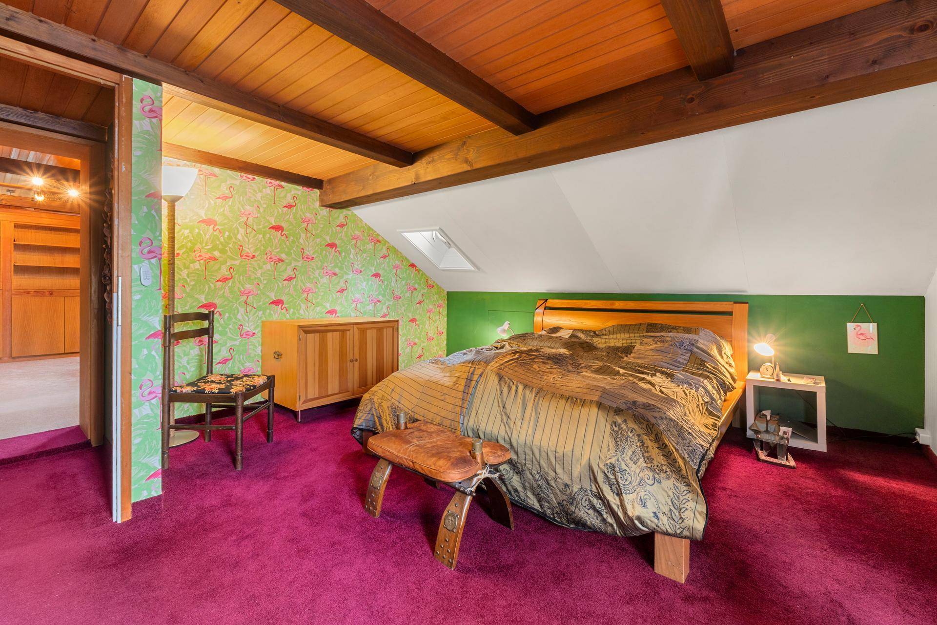 Schlafzimmer im Dachgeschoss mit farbenfroher Flamingo-Tapete, Holzbalken und Dachfenster.