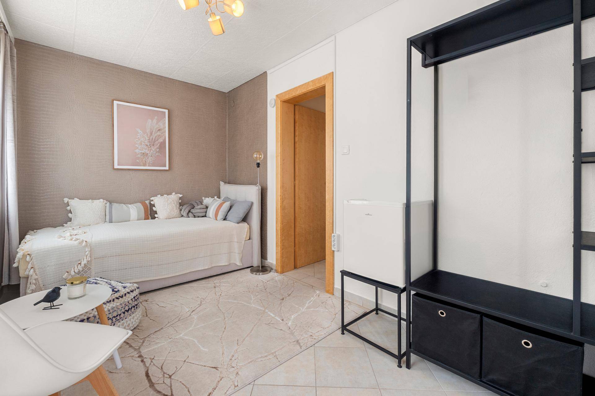 Helles Zimmer mit Tagesbett, kleinem Kühlschrank und offenem Kleiderschrank, ideal als Gästezimmer.
