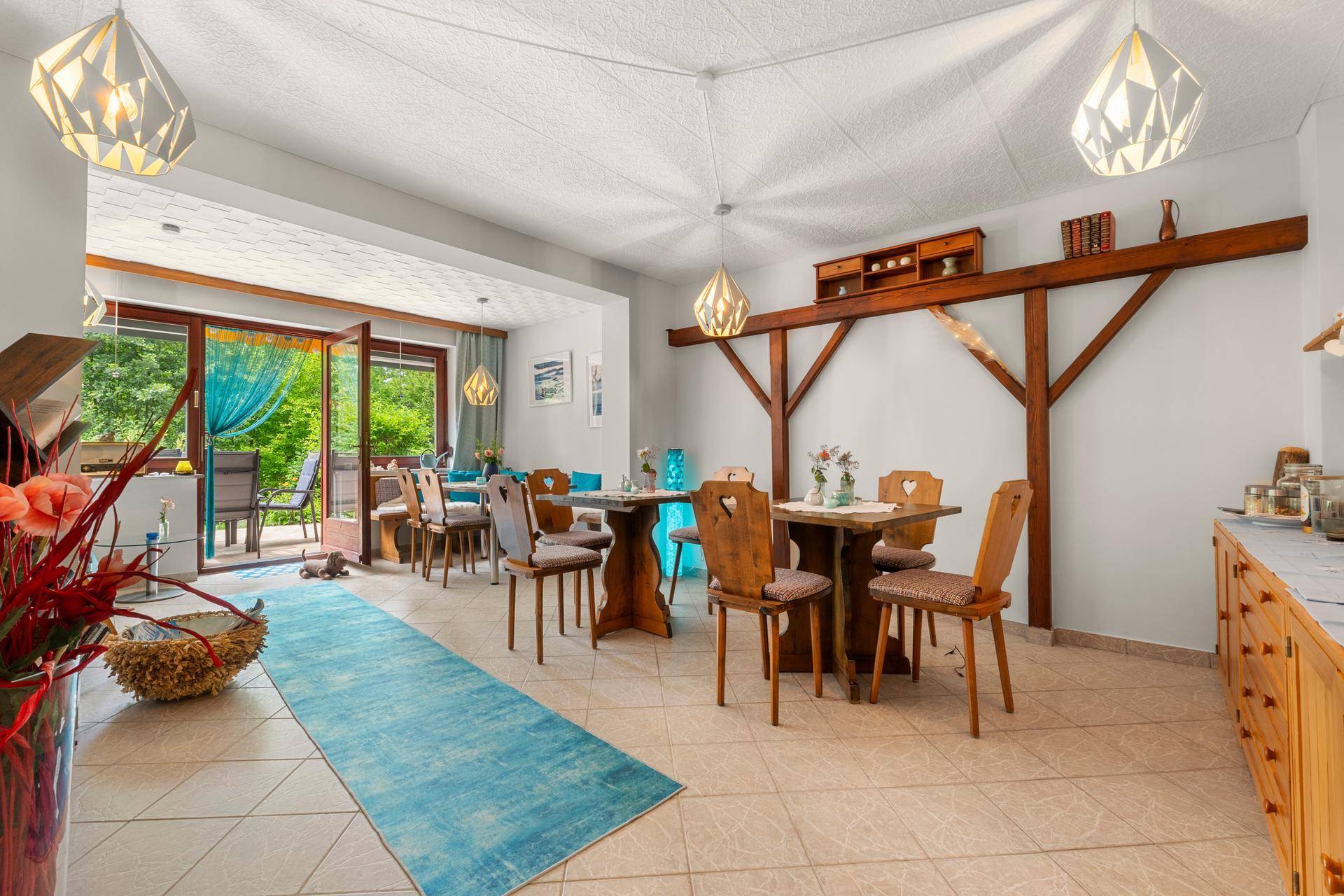 Rustikaler Essbereich mit Holztischen, Stühlen und Zugang zu einer Terrasse mit Gartenblick.