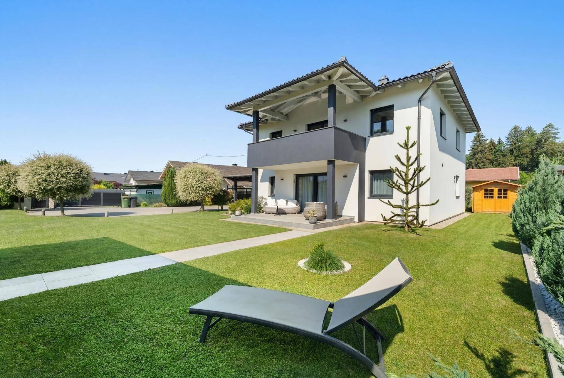 Weitläufiger Garten mit Liegestuhl und modernem Einfamilienhaus im Hintergrund, ideal zum Entspannen.