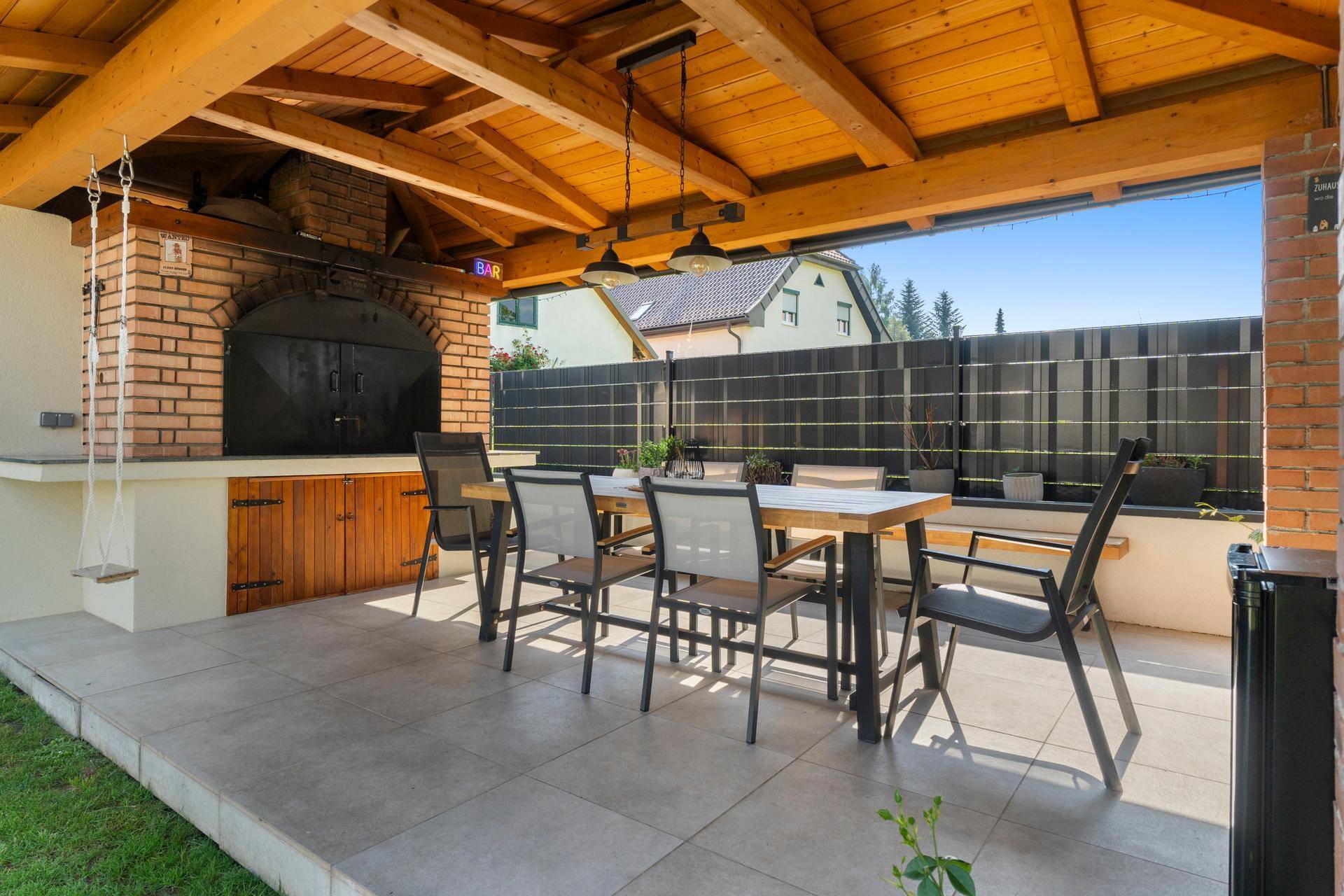 Überdachte Terrasse mit großem Esstisch, Außenküche und Grill, perfekt für gesellige Abende.