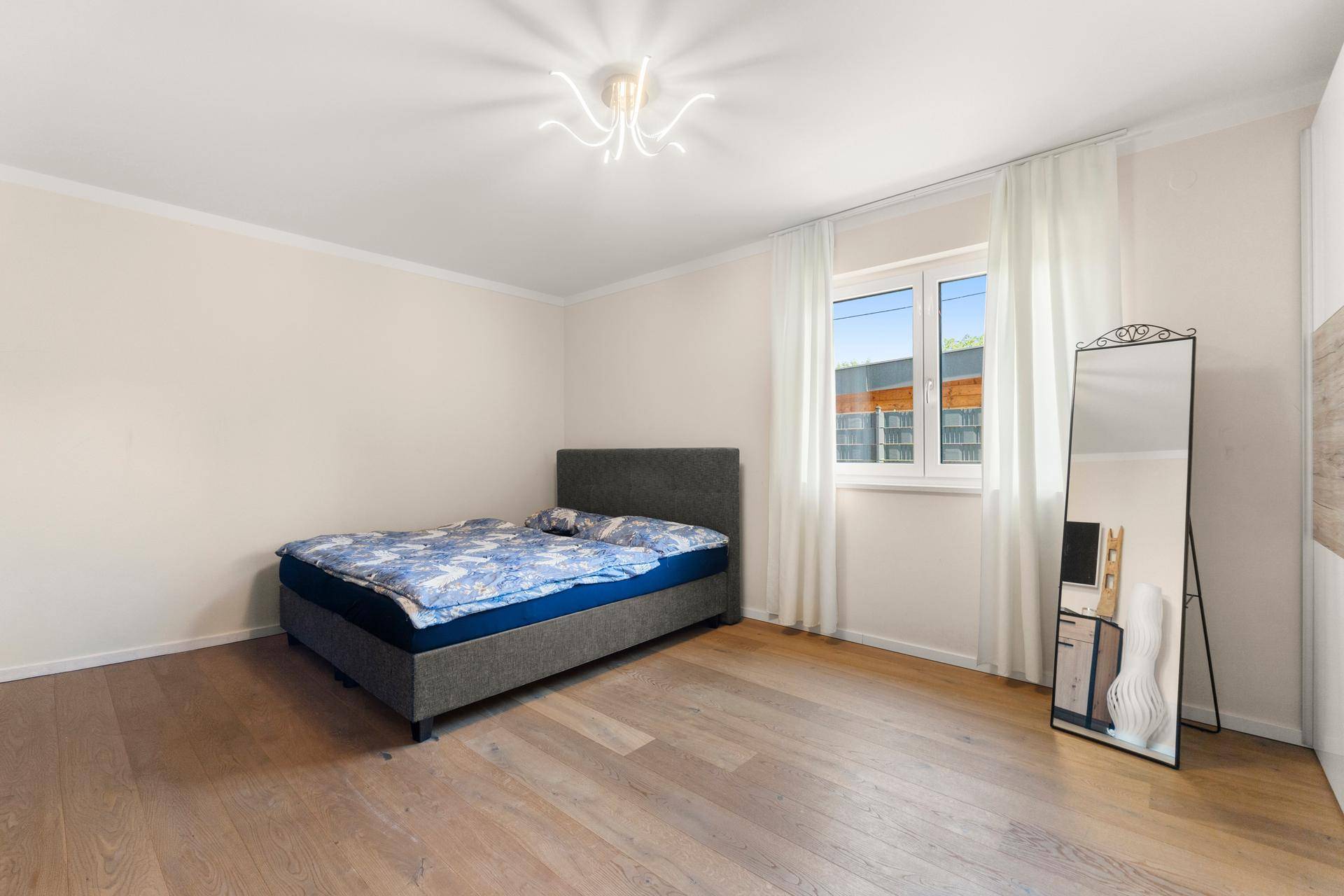 Helles Schlafzimmer mit Holzboden, großem Fenster und modernem Bett.