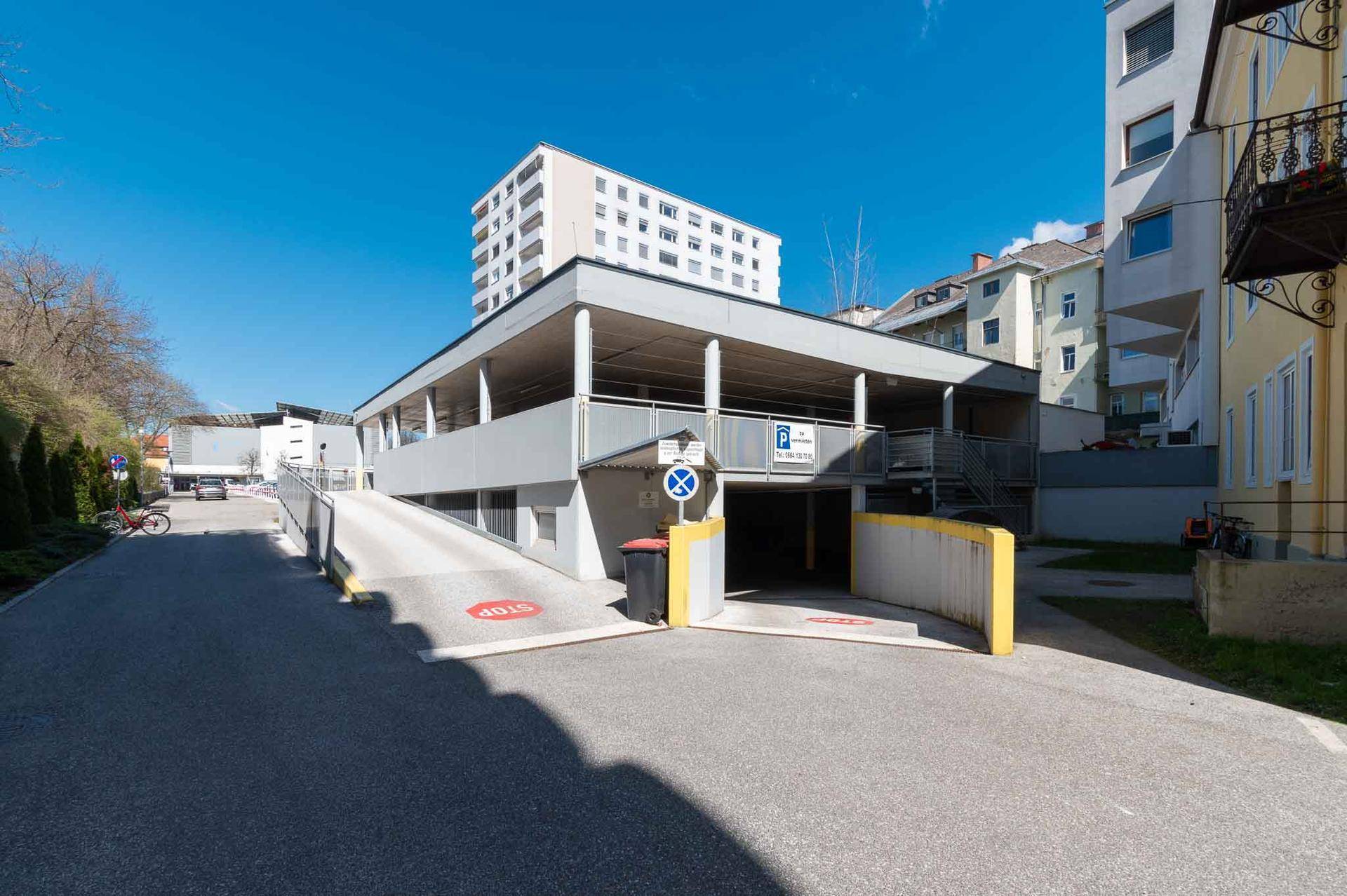 Einfahrt zu einem mehrstöckigen Parkhaus mit Rampe und umliegenden Gebäuden.