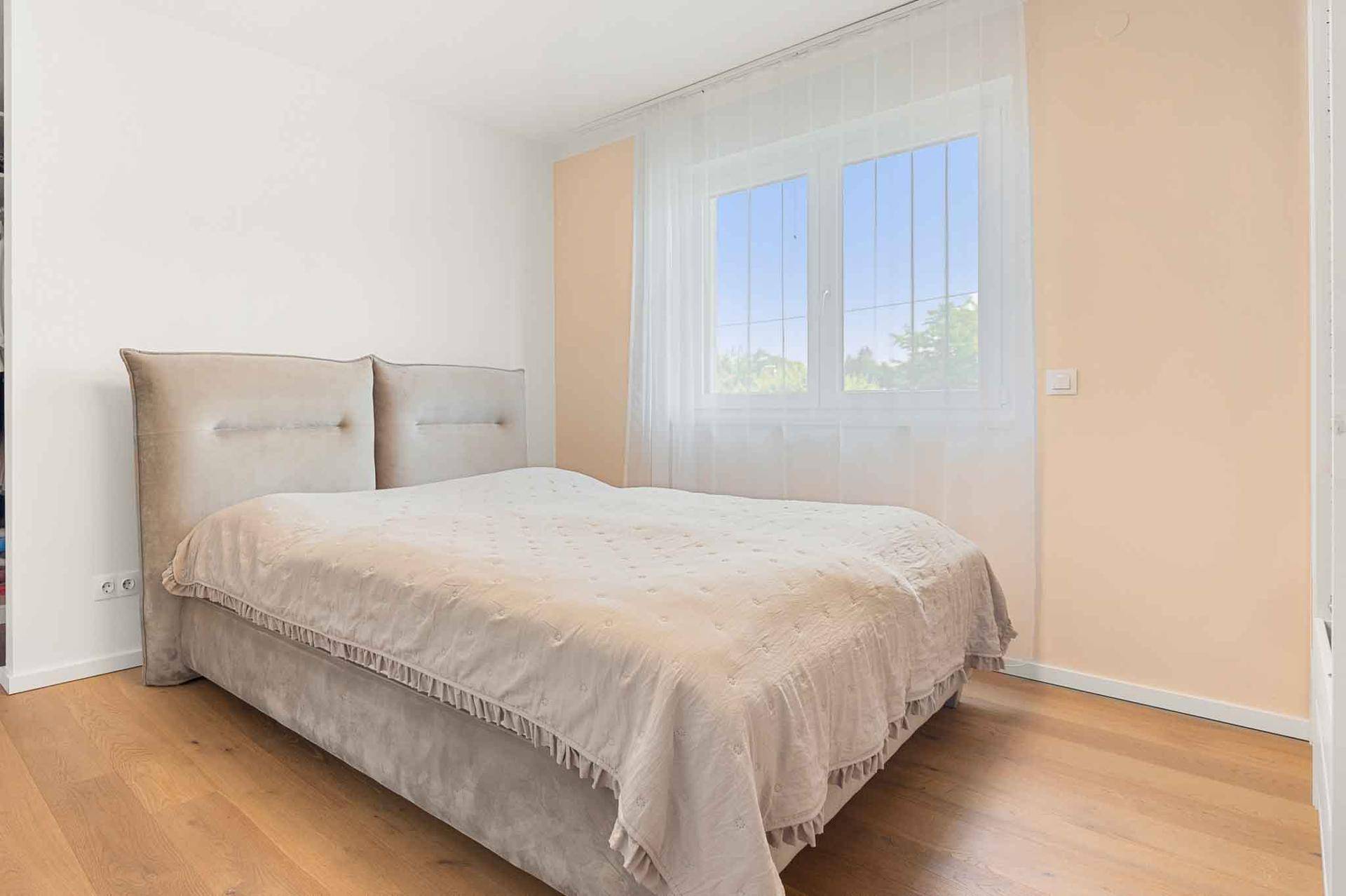 Gemütliches Schlafzimmer mit Doppelbett, Holzboden und einem großen Fenster für viel Tageslicht.