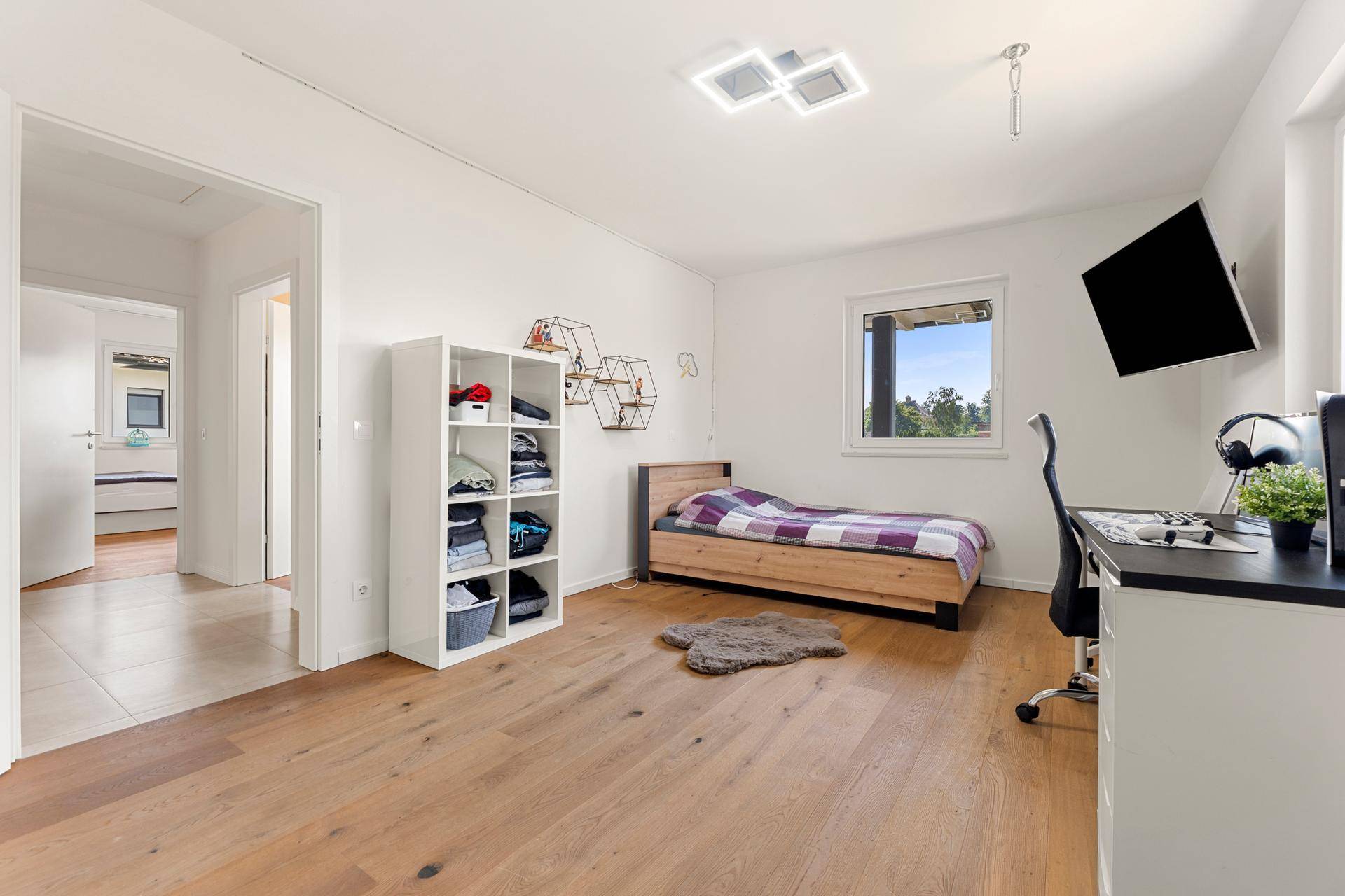 Kinderzimmer mit Holzboden, Einzelbett, Schreibtisch und einem Regal, hell und funktional eingerichtet.