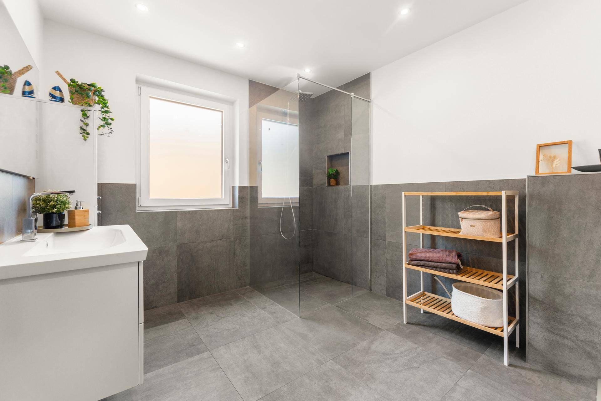 Modernes Badezimmer mit begehbarer Dusche, grauen Fliesen und Fenster.