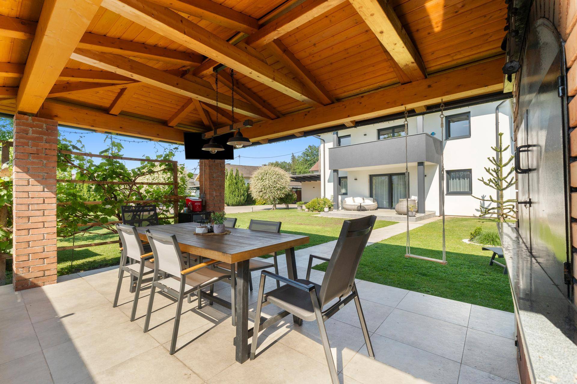 Gemütliche überdachte Terrasse mit Esstisch und Blick auf den Garten und das moderne Haus.