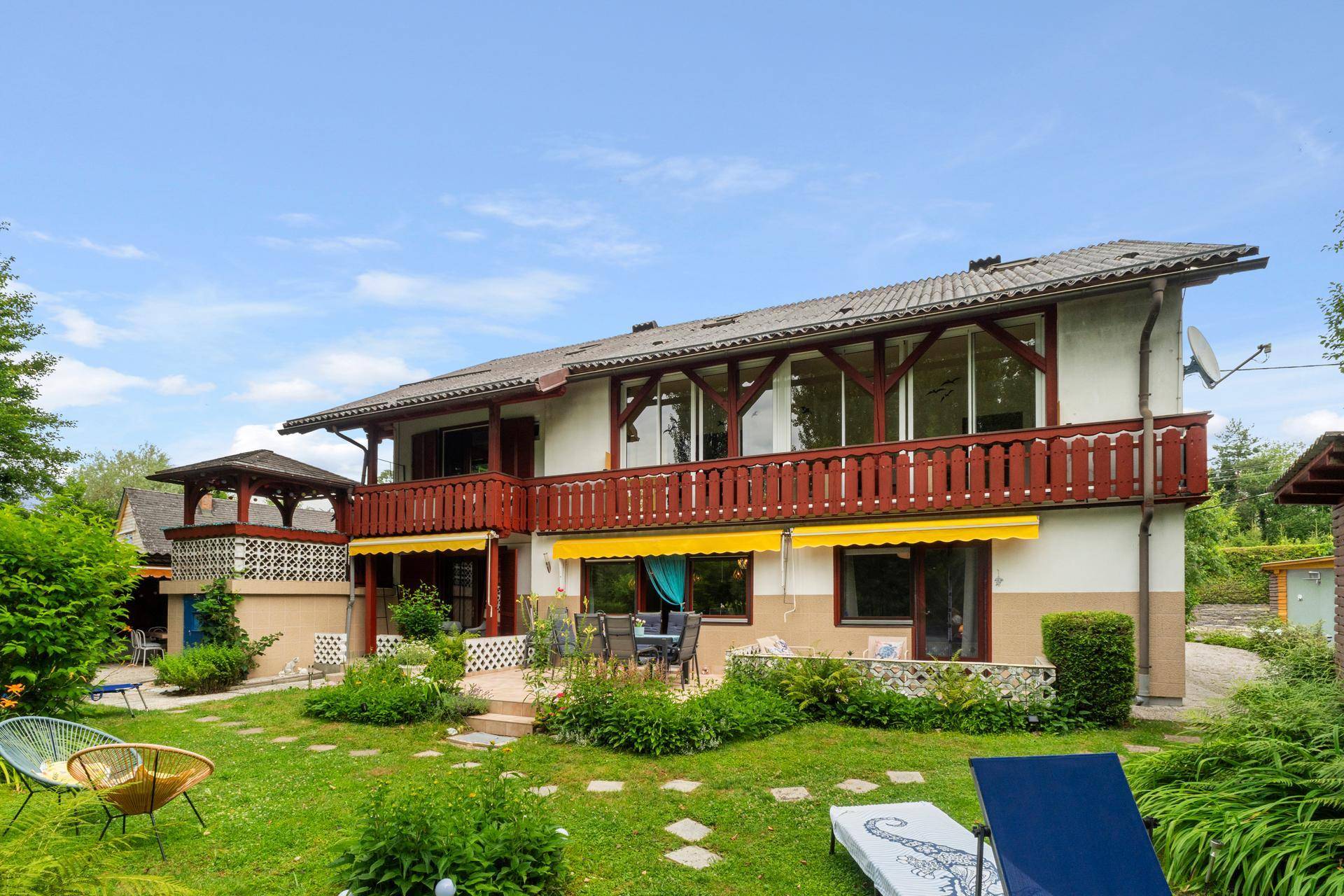 Großer Garten mit Rasenfläche, Sonnenliegen und einer Terrasse vor dem Haus mit Balkonen.