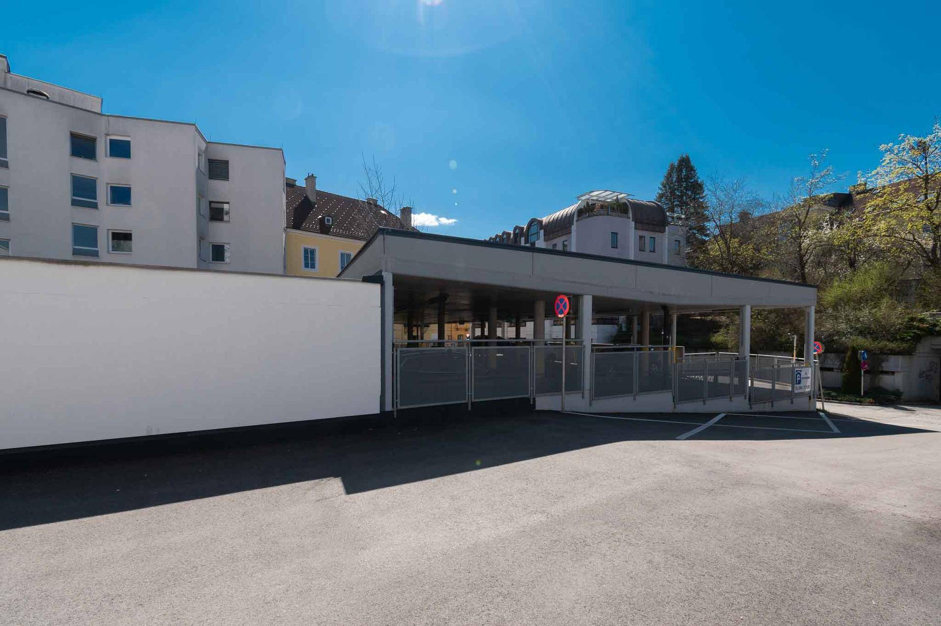 Seitenansicht des Parkhauses mit einer langen weißen Wand und weiteren Gebäuden im Hintergrund.