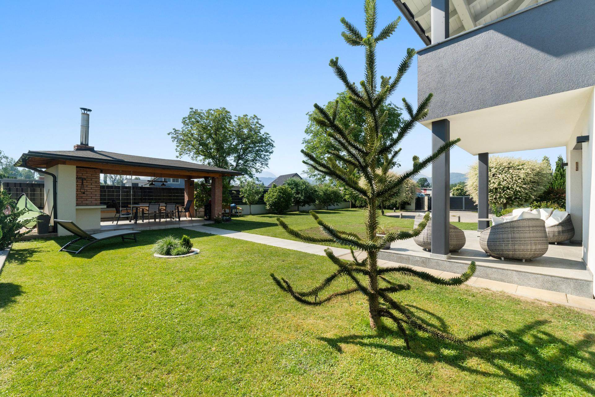 Großer Garten mit Rasenfläche und überdachtem Essbereich mit Außenküche und Grill.
