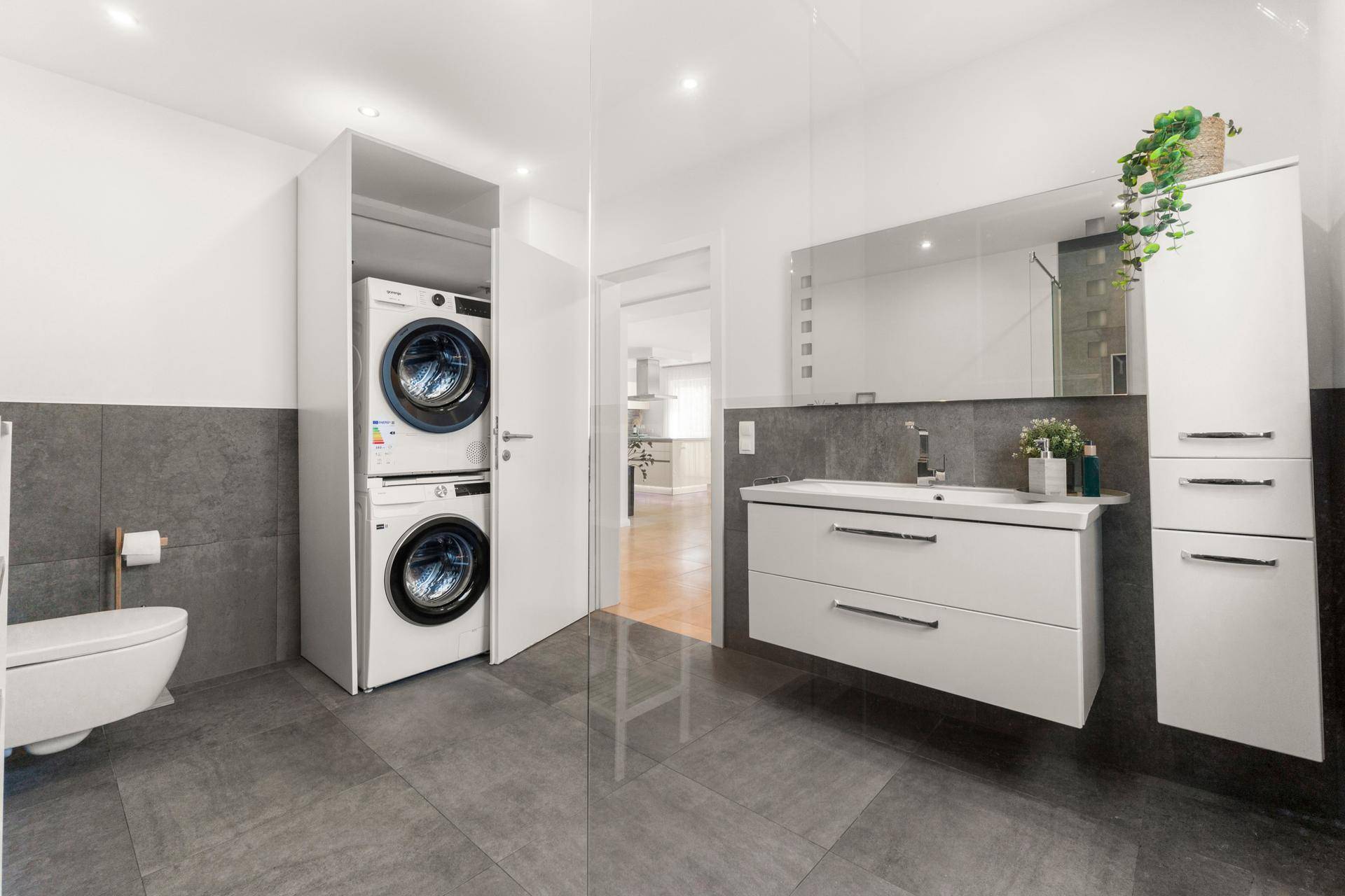 Funktionales Badezimmer mit Toilette, Waschtisch und integriertem Waschmaschinen-Trockner-Turm.