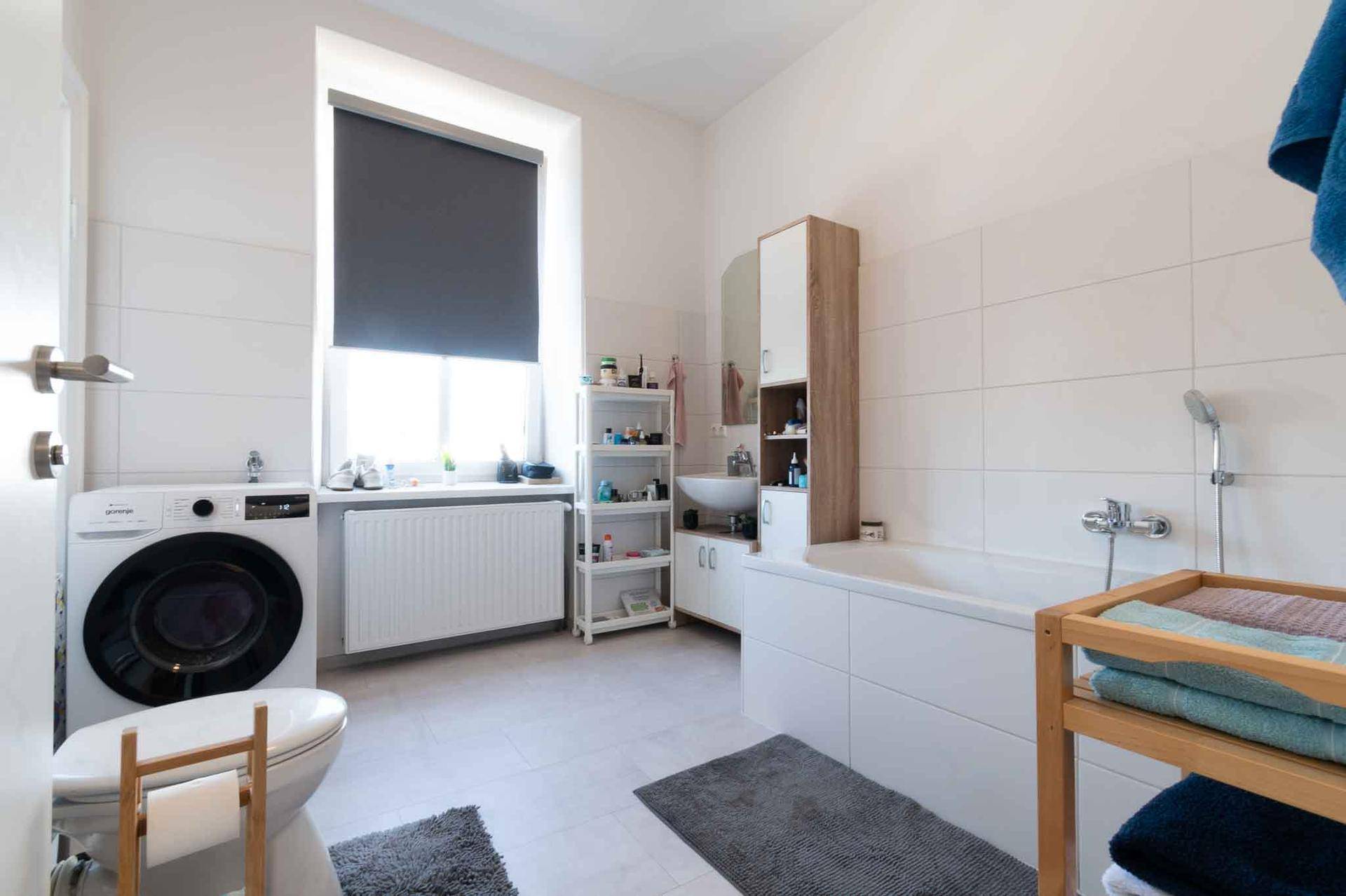 Modernes Badezimmer mit Badewanne, Waschmaschine und Fenster für natürliche Belüftung.