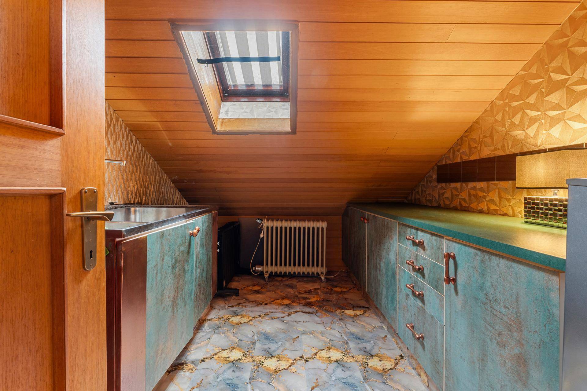 Kleine Küche im Dachgeschoss mit Holzverkleidung, Spüle und Heizkörper unter dem Dachfenster.