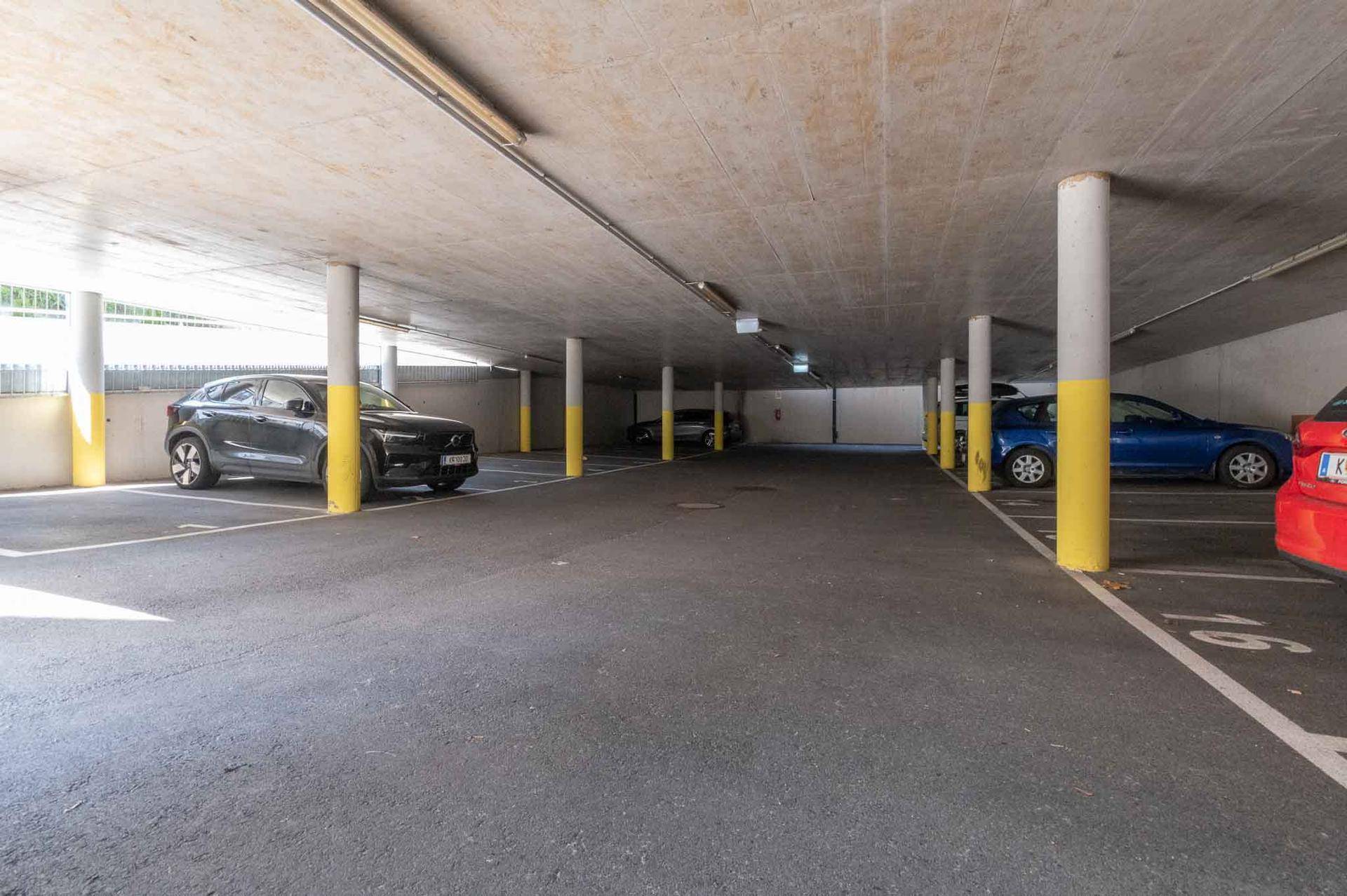 Helle Tiefgarage mit zahlreichen Parkplätzen, gelben Säulen und geparkten Fahrzeugen.