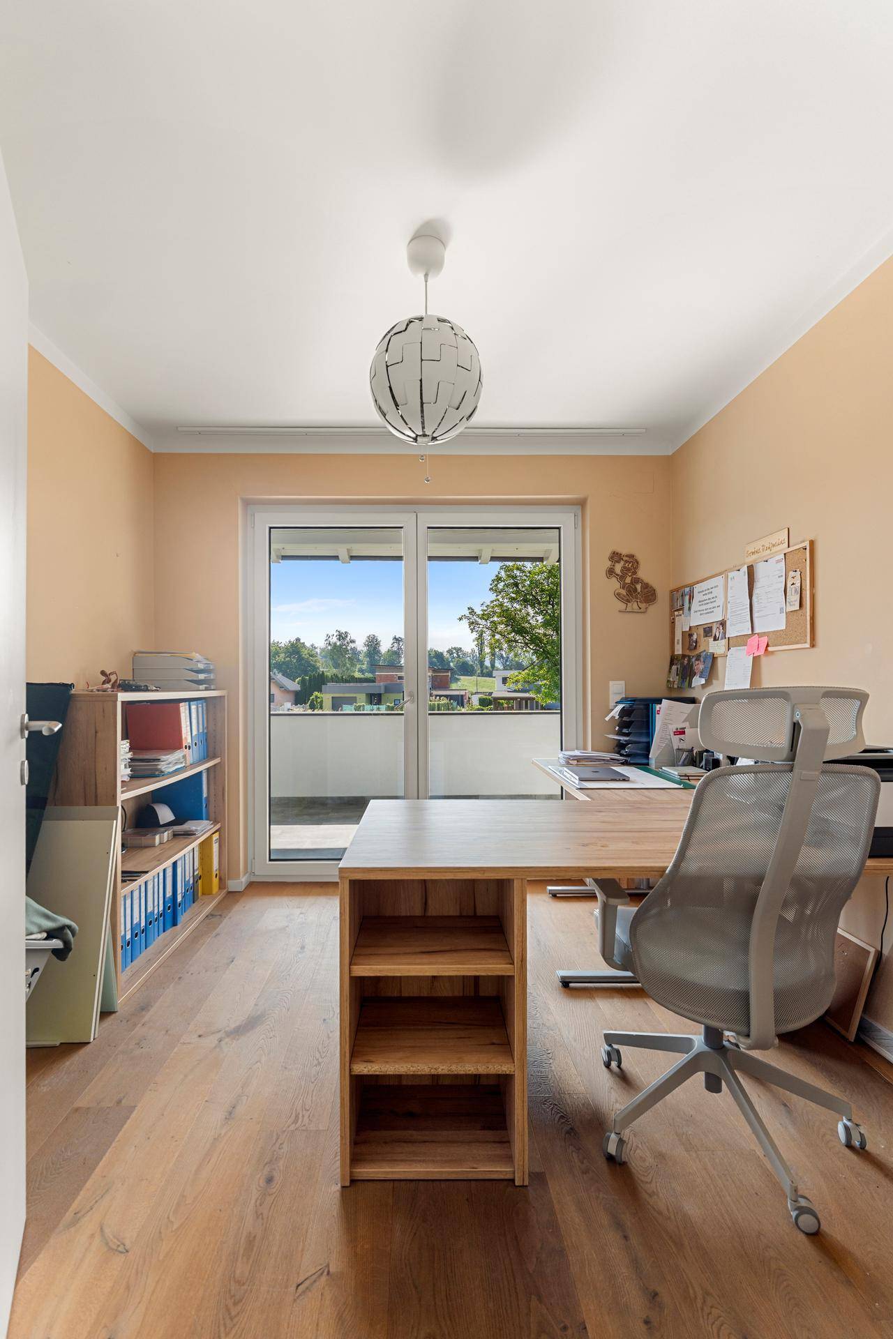 Helles Arbeitszimmer mit Holzboden, Schreibtisch und Zugang zu einem Balkon, ideal für Home-Office.