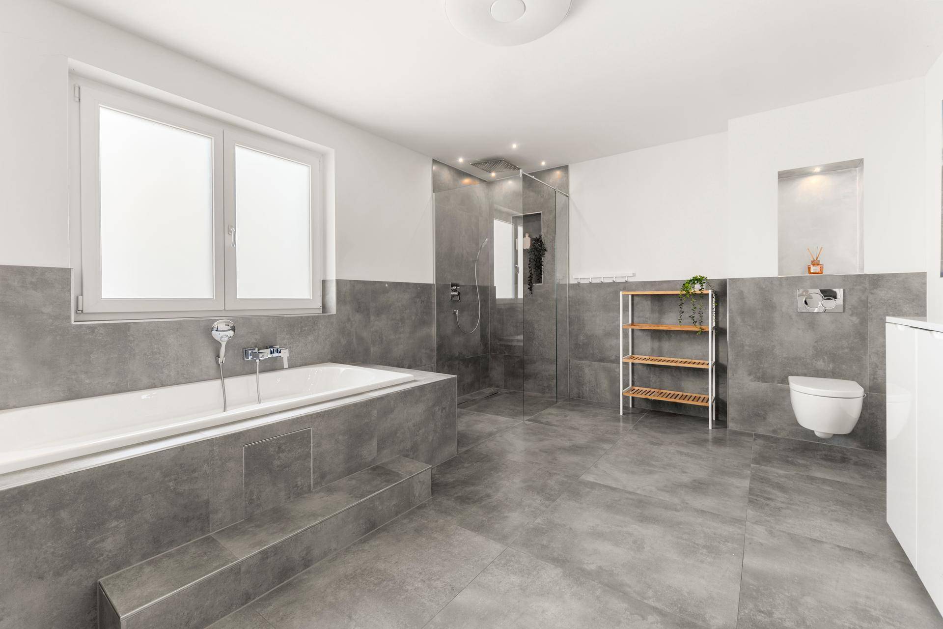 Modernes Badezimmer mit großer Badewanne, ebenerdiger Dusche und grauen Fliesen, sehr geräumig.