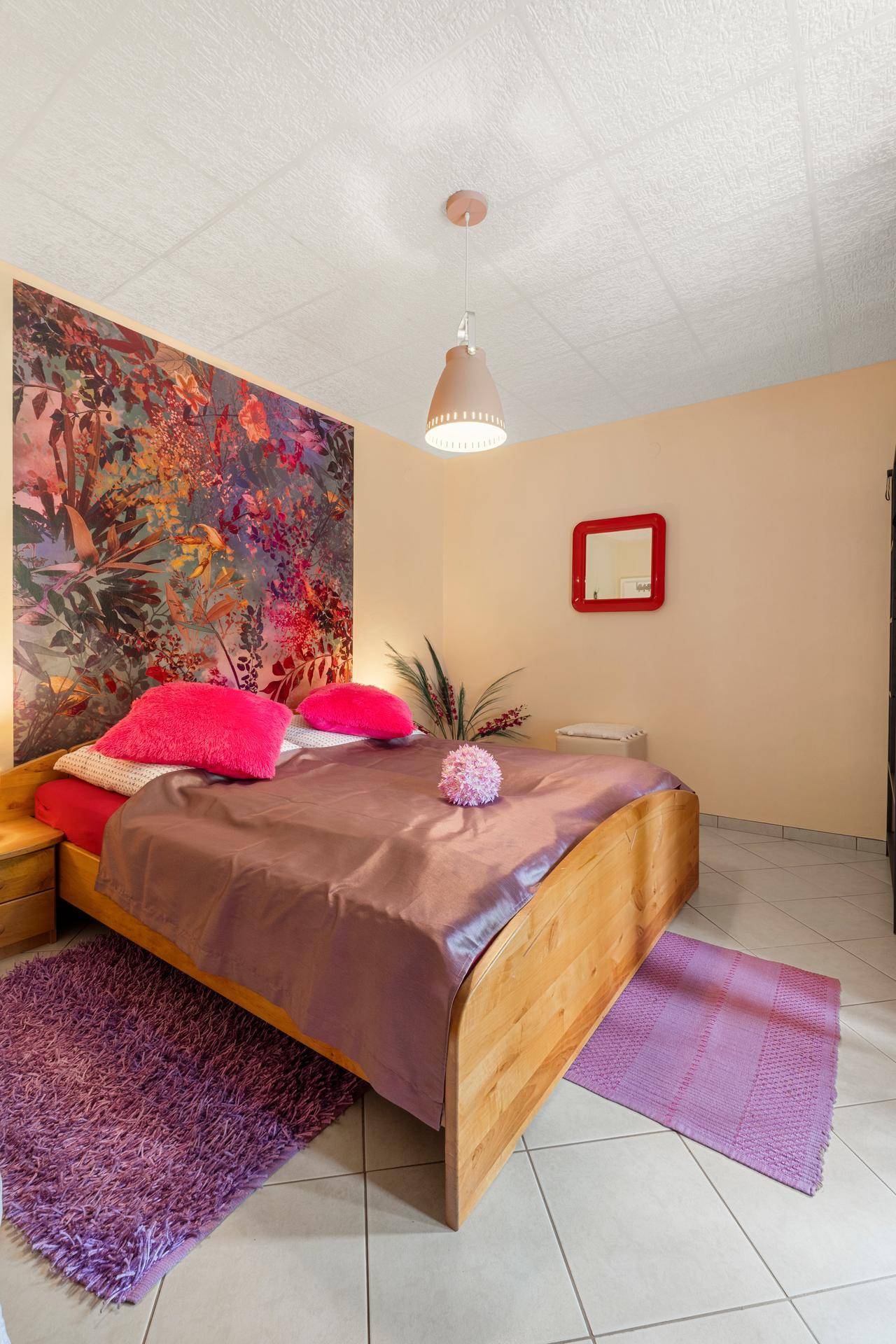Helles Schlafzimmer mit farbenfroher Tapete, großem Bett und Fliesenboden.