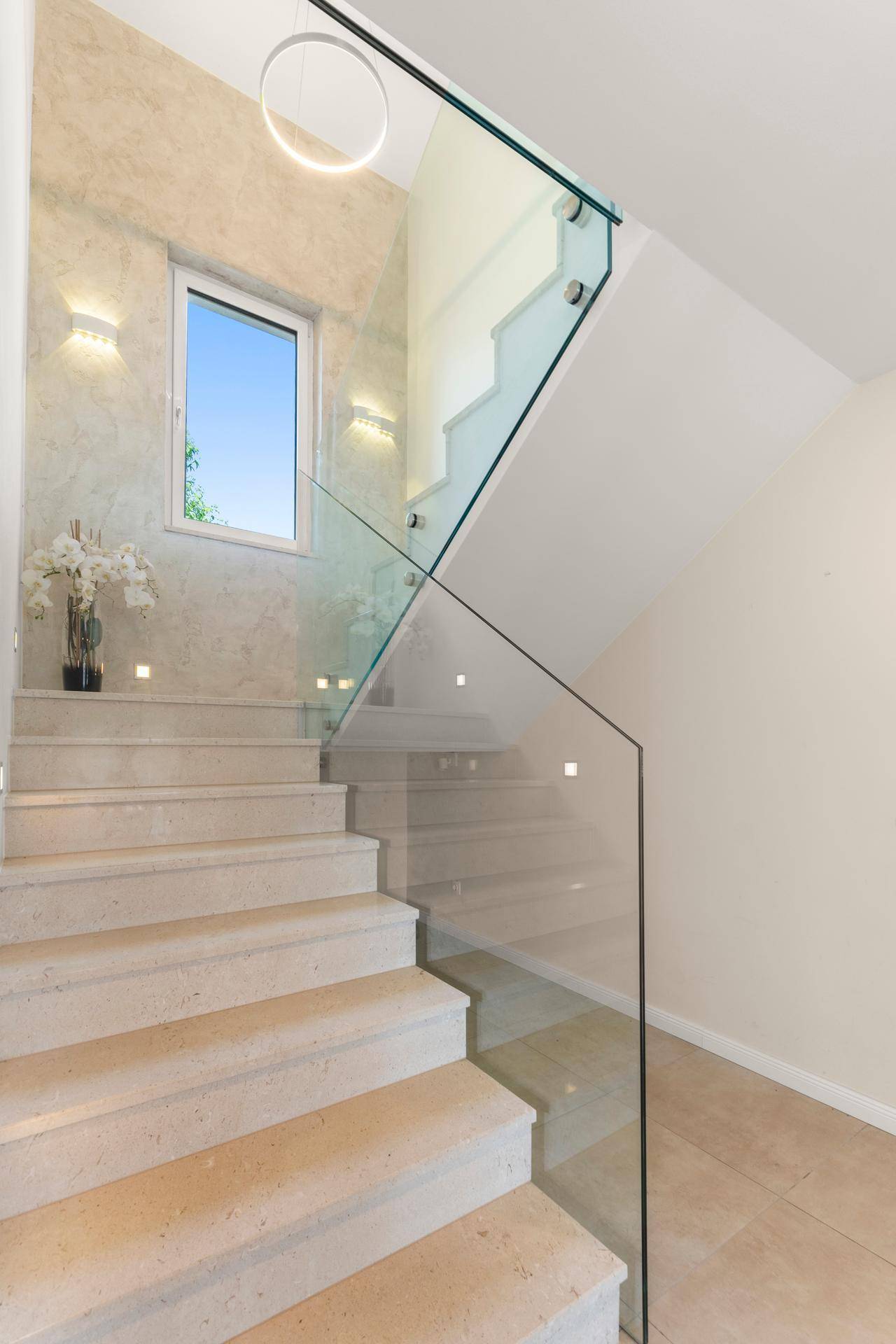 Elegantes Treppenhaus mit Glasgeländer, Natursteinstufen und natürlichem Lichteinfall.