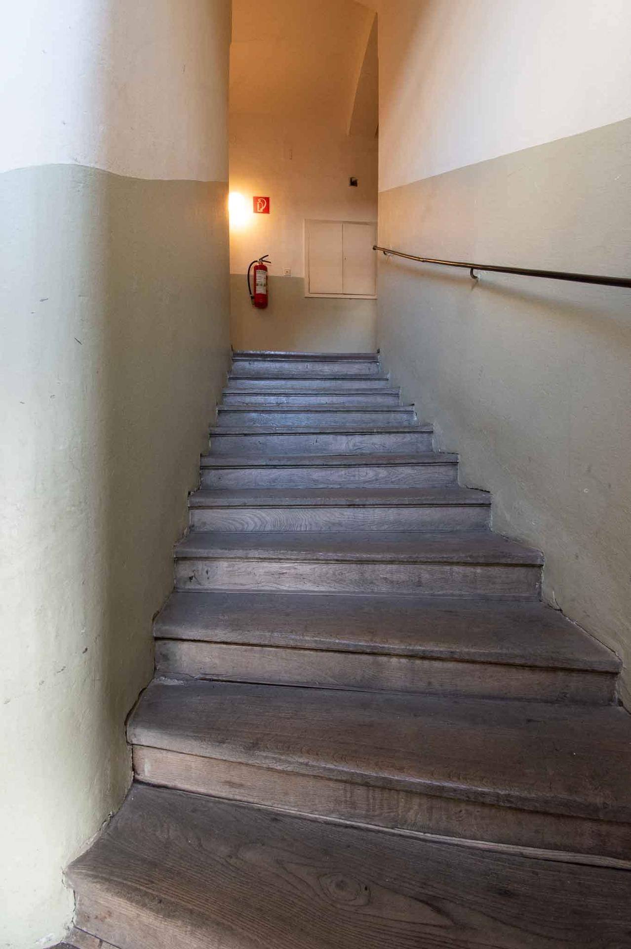 Holztreppe in einem Flur mit zweifarbigen Wänden und einem Feuerlöscher an der Wand.