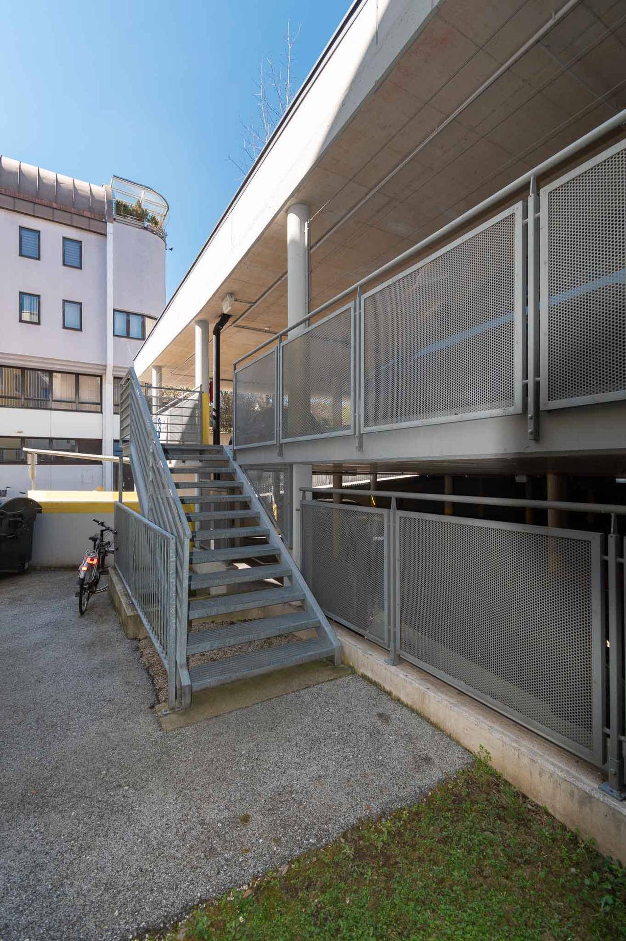 Metalltreppe führt zu einer oberen Parkebene, umgeben von perforierten Metallgeländern.