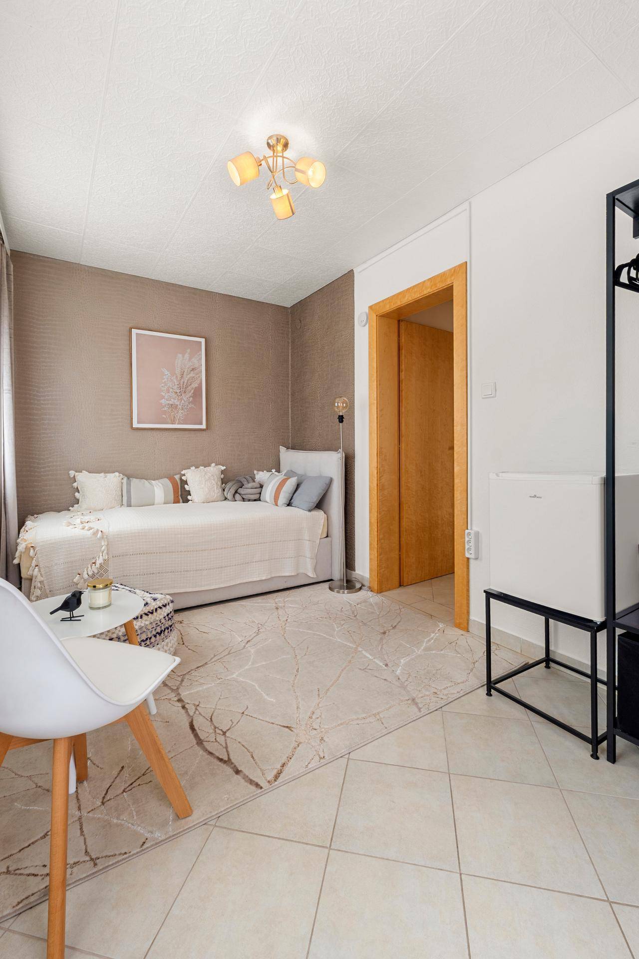 Gemütliches Zimmer mit Tagesbett, beiger Tapete und Fliesenboden, gut beleuchtet.