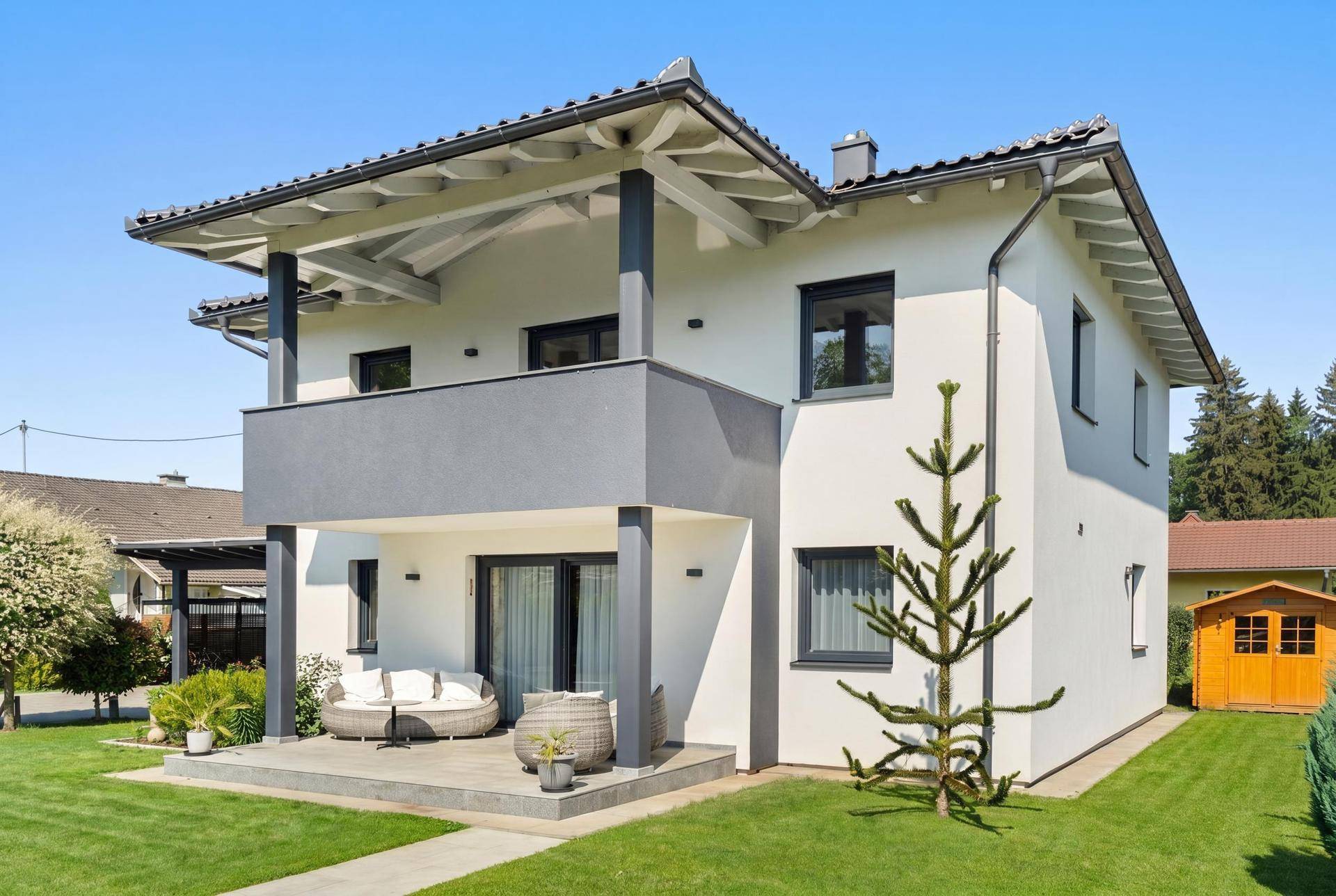 Modernes Einfamilienhaus mit Terrasse, Balkon und gepflegtem Rasen, umgeben von viel Grün.