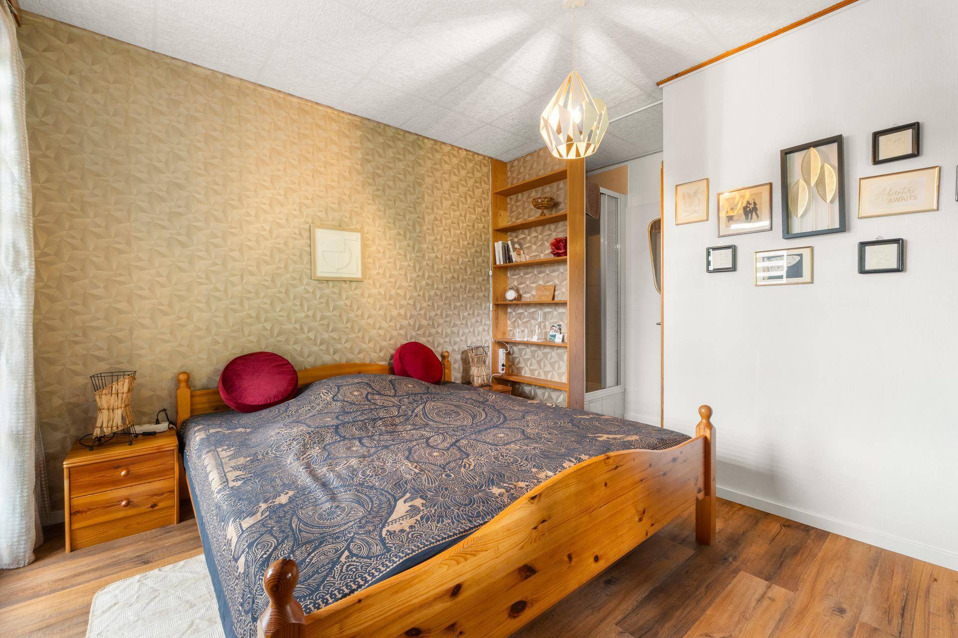 Schlafzimmer mit Holzbett, gemusterter Tapete und Duschbereich, teilweise mit Holzboden.