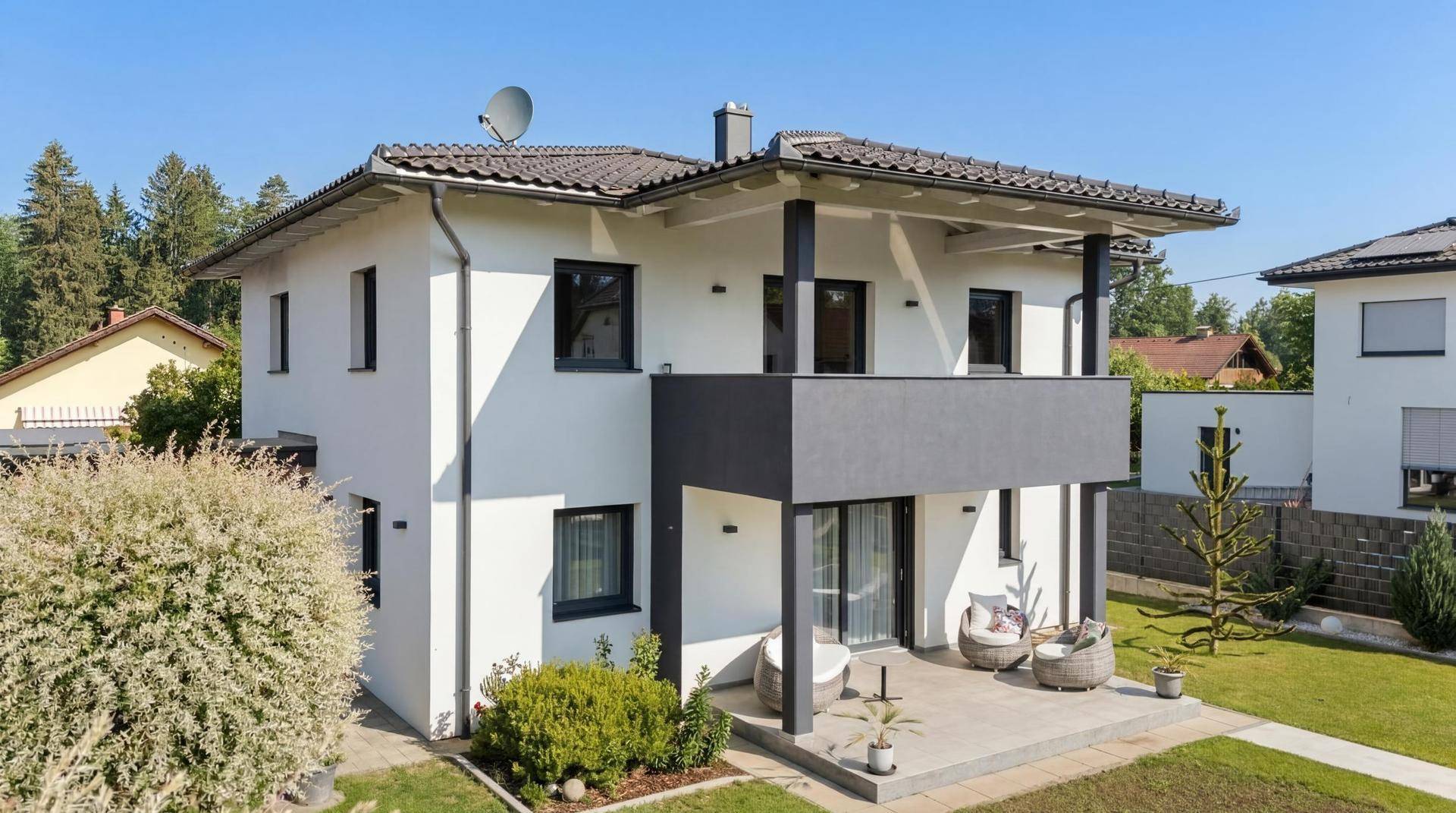 Vorderansicht des modernen Hauses mit Balkon und kleiner Terrasse mit Sitzgelegenheiten.