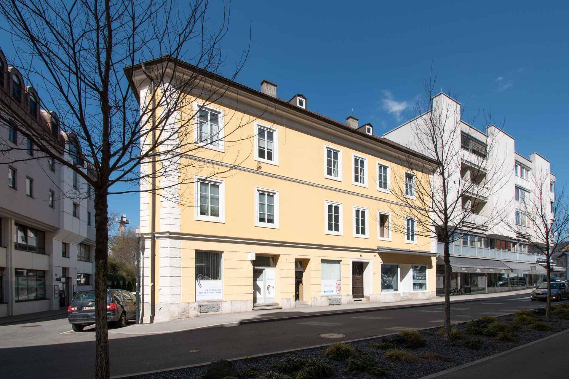 Historisches Gebäude mit gelber Fassade und weißen Fenstern an einer belebten Straße.