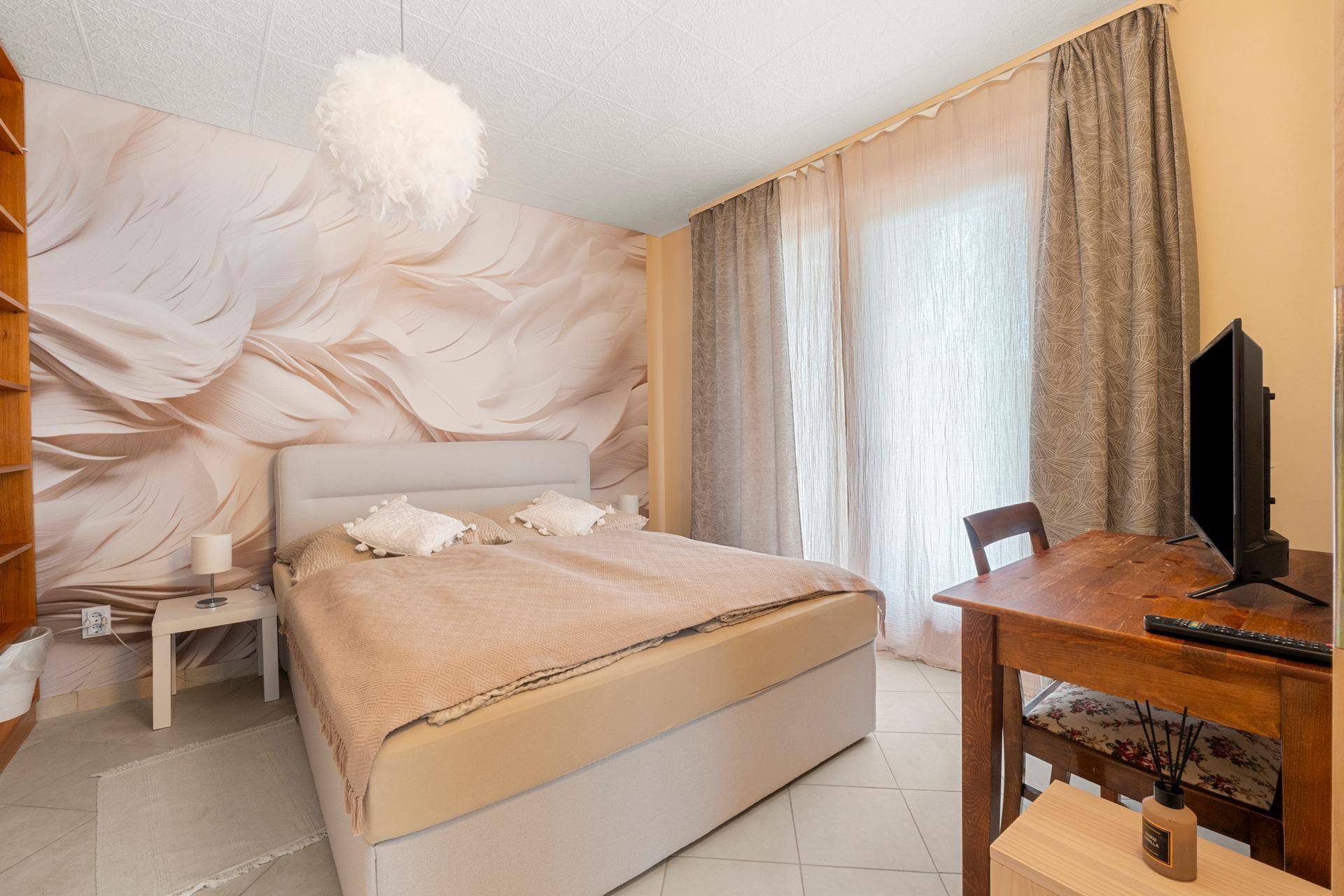 Schlafzimmer mit Doppelbett, Holzregal und gemusterter Tapete, hell durch großes Fenster.