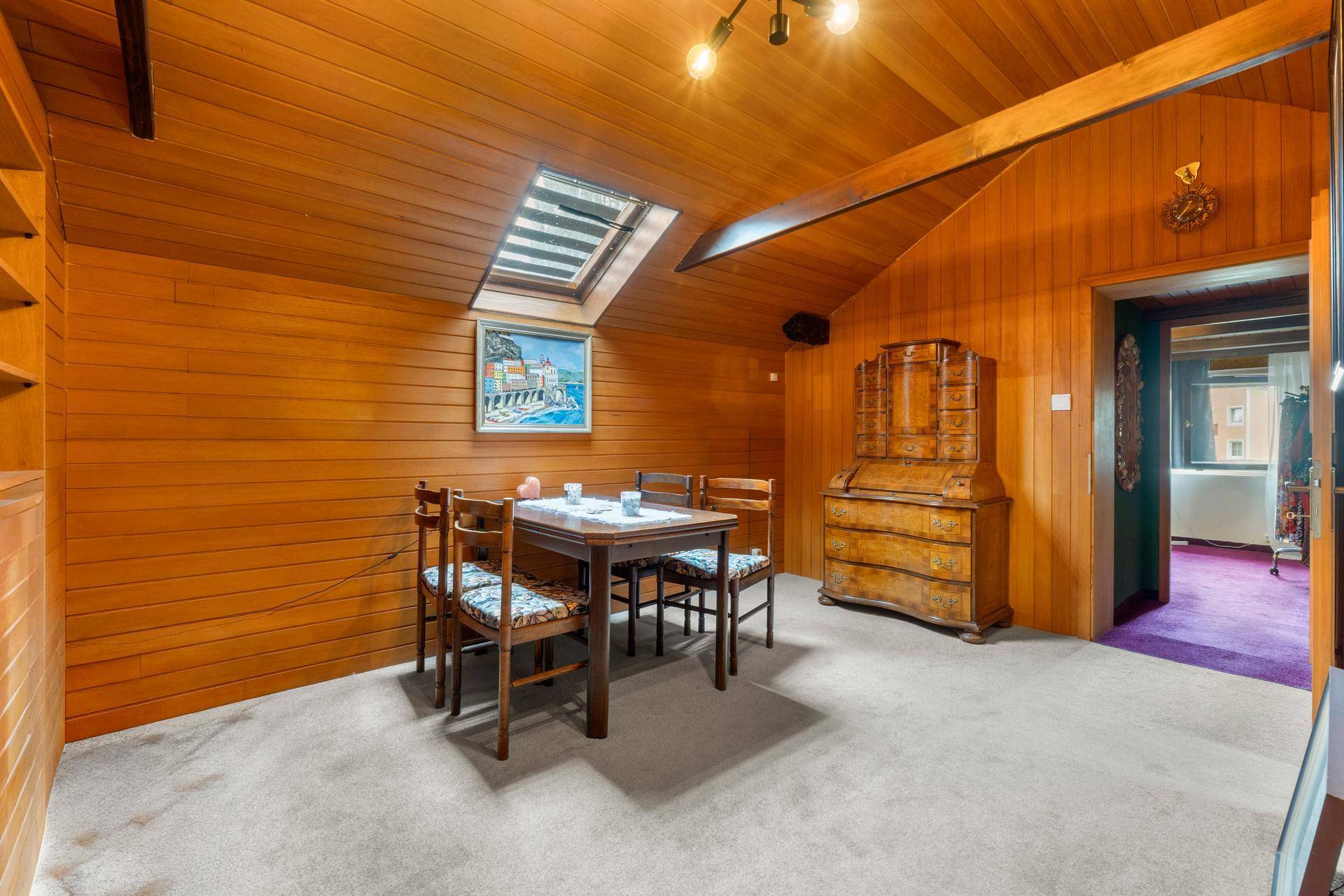 Essbereich im Dachgeschoss mit Holzverkleidung, Esstisch und Dachfenster für natürliches Licht.