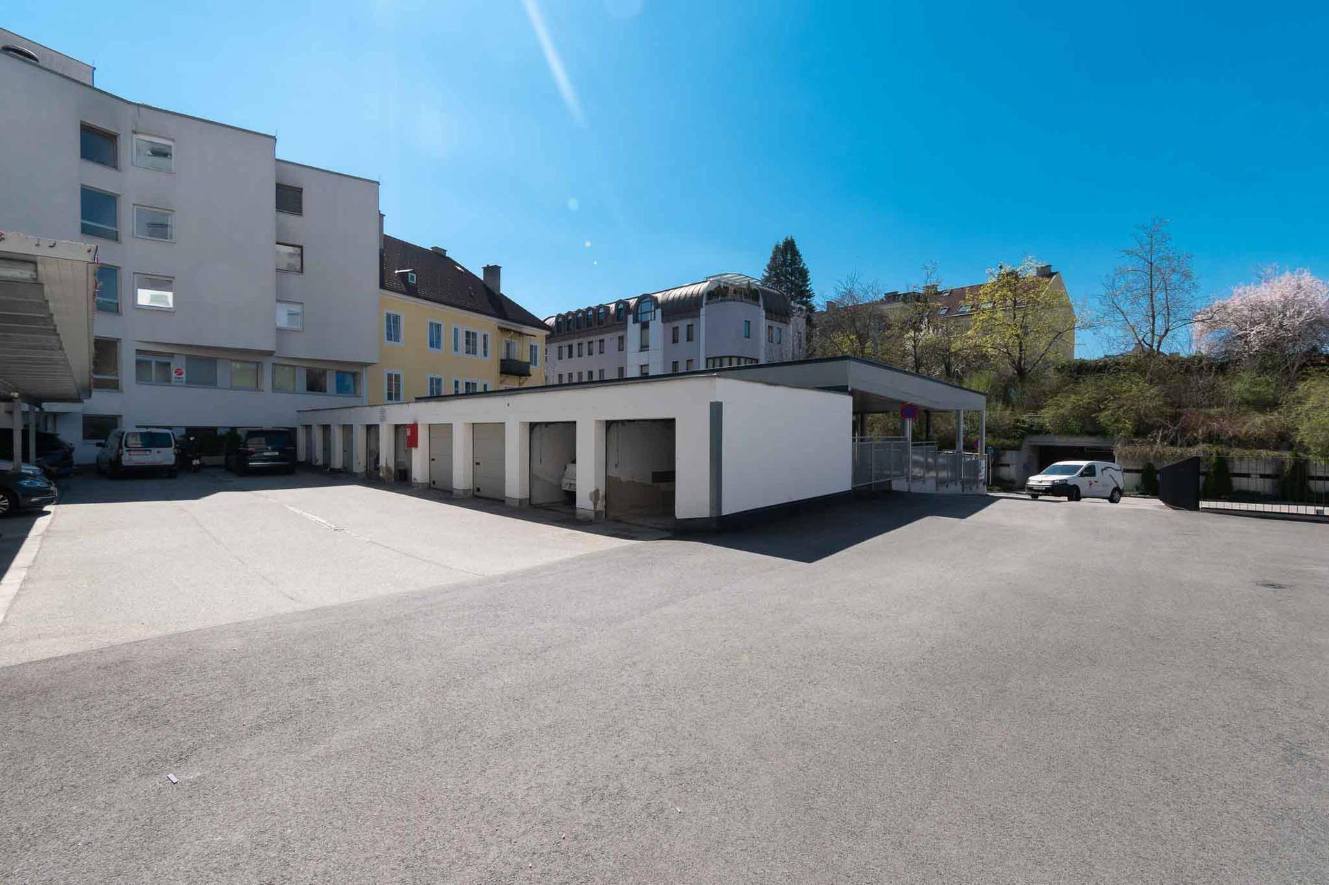 Außenparkplätze und Garagenboxen neben einem Gebäude unter strahlend blauem Himmel.