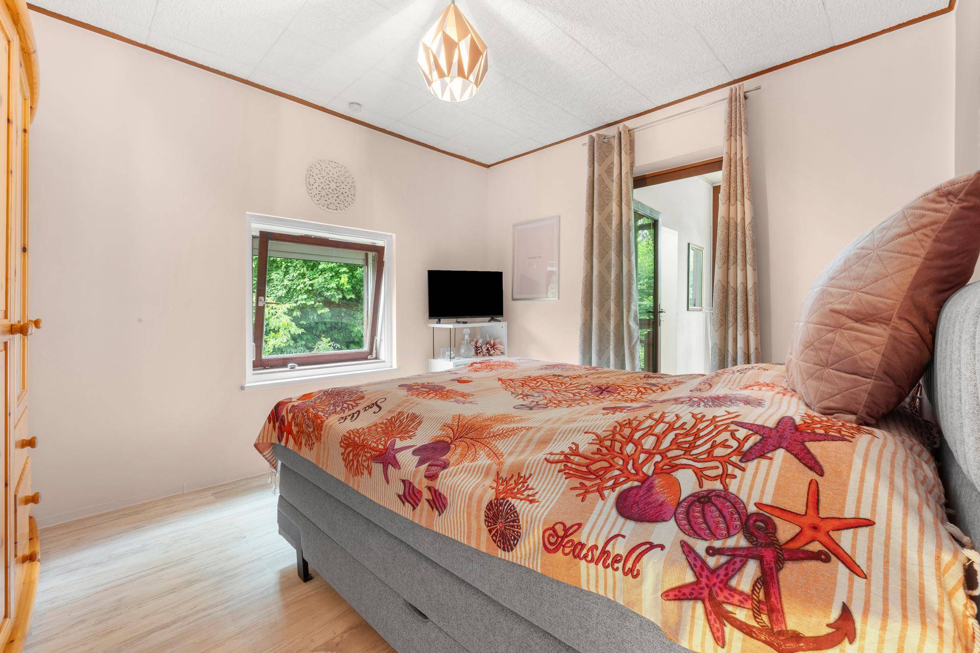 Gemütliches Schlafzimmer mit Doppelbett, Holzschrank und Fenster mit Blick ins Grüne.
