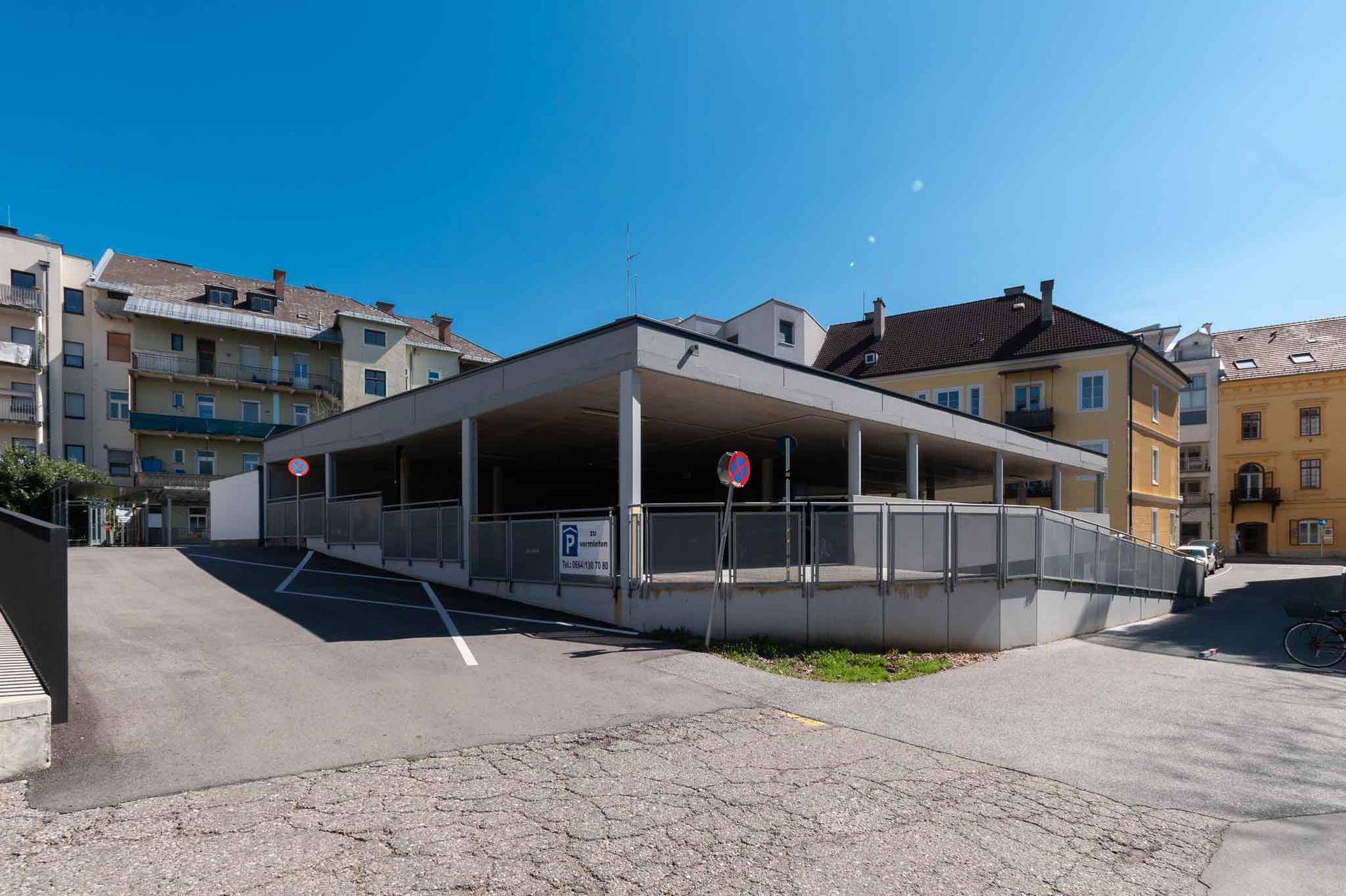 Offenes Parkhaus mit mehreren Ebenen und einer Zufahrtsrampe unter blauem Himmel.