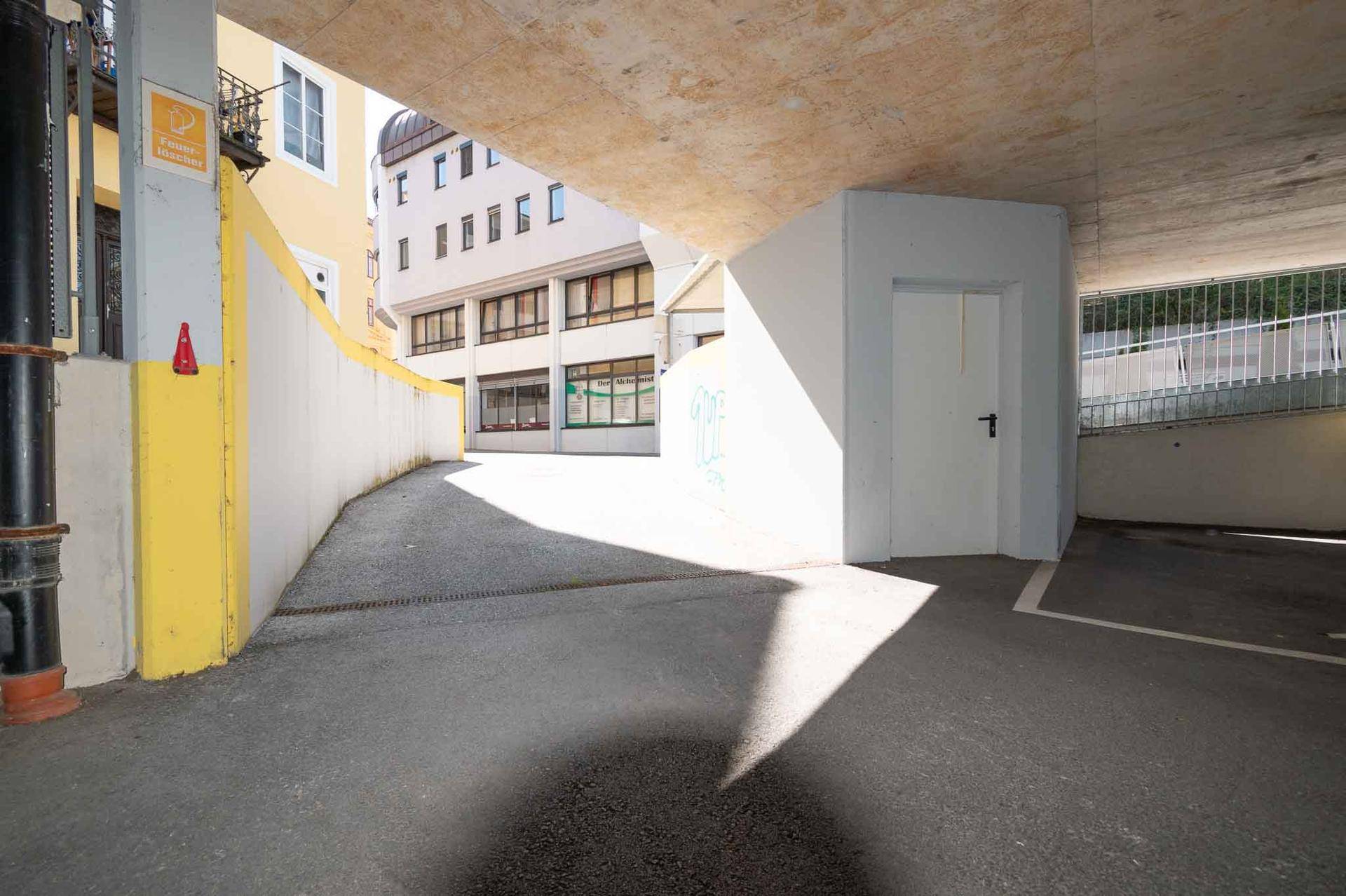 Zufahrtsbereich in einem Parkhaus mit gelb-weißen Wänden und einem kleinen Raum.