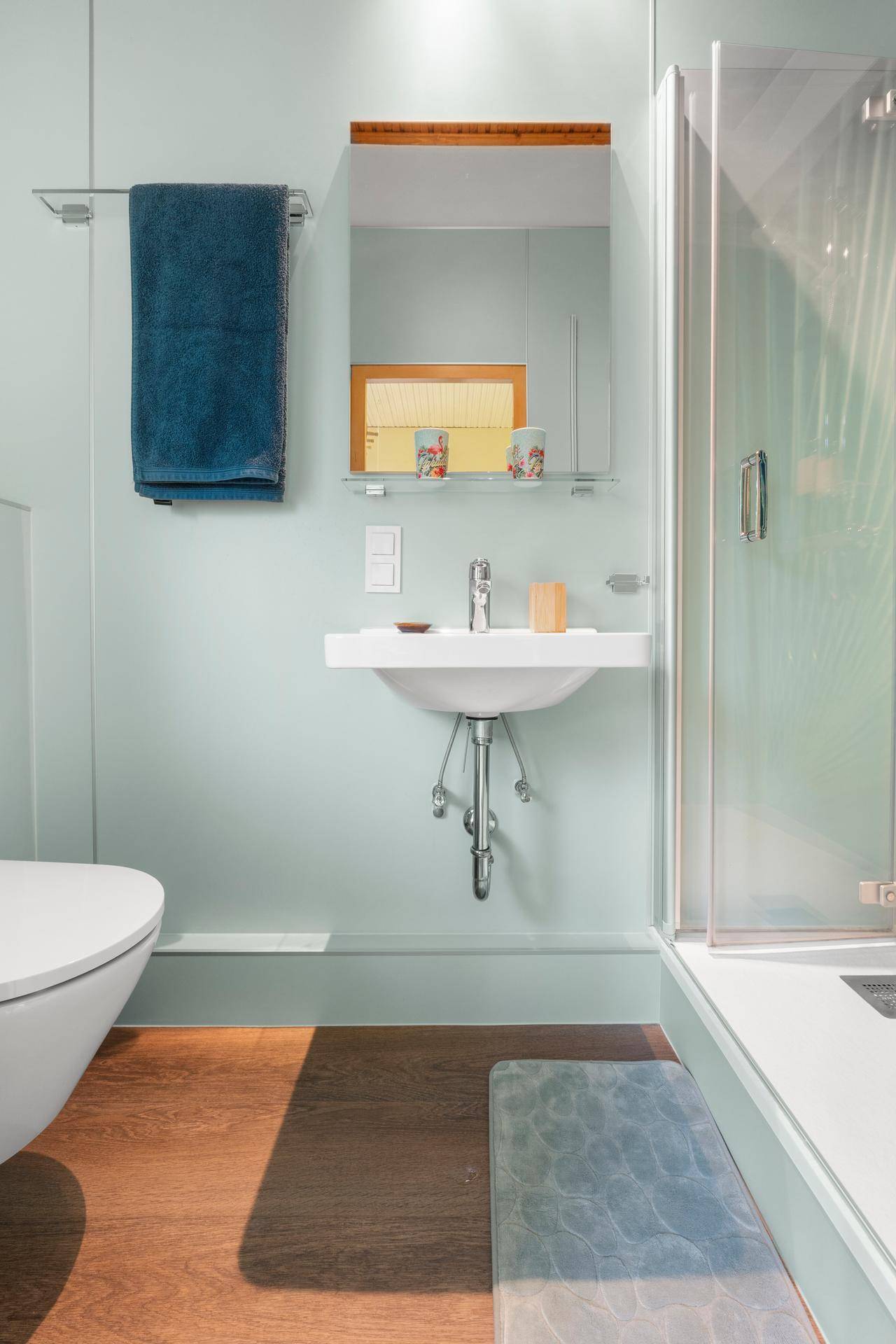 Modernes Badezimmer mit Dusche, Hänge-WC und Einzelwaschbecken, hellblau gestrichen.