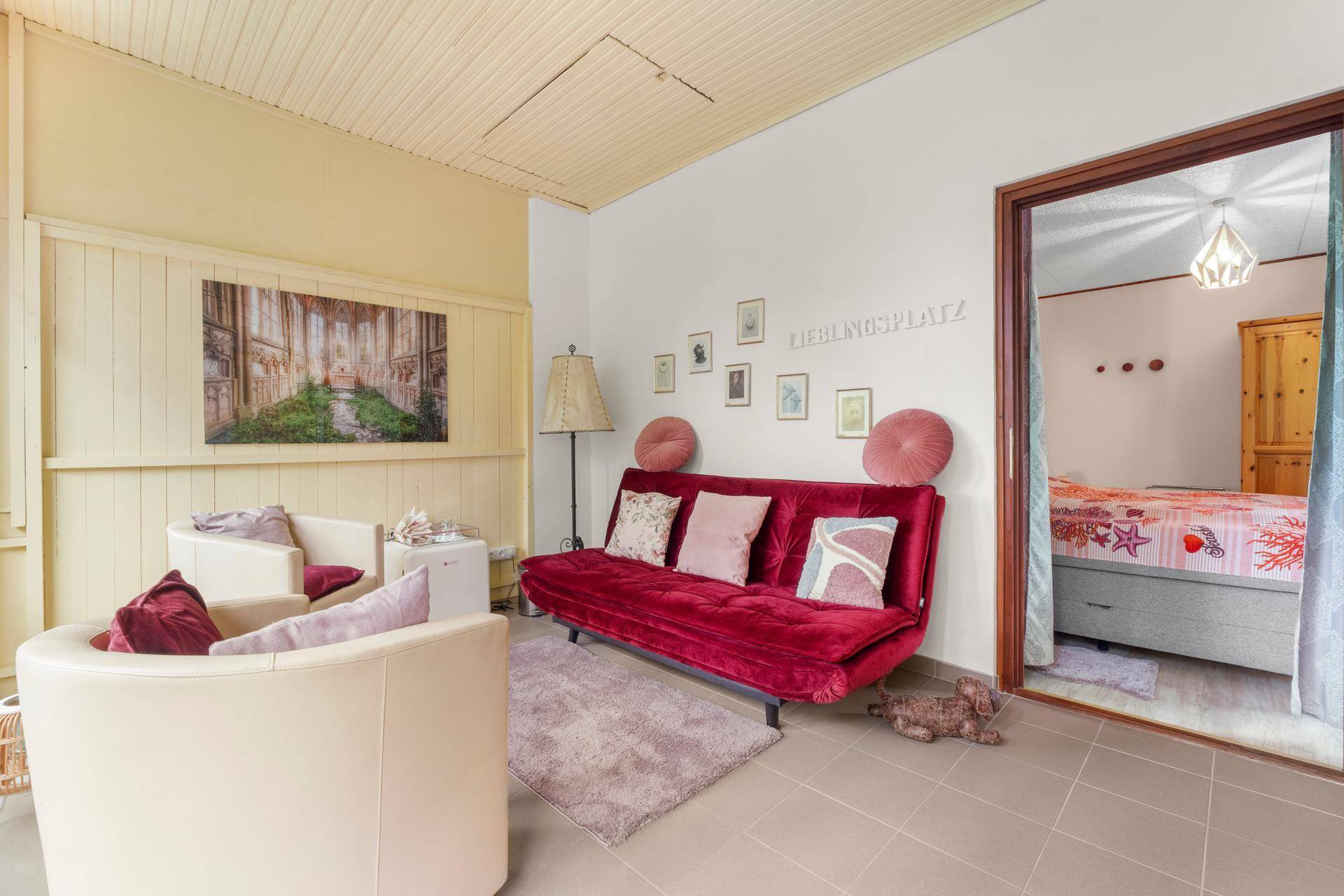 Wohnzimmer mit rotem Sofa, bequemen Sesseln und Zugang zu einem weiteren Schlafzimmer.
