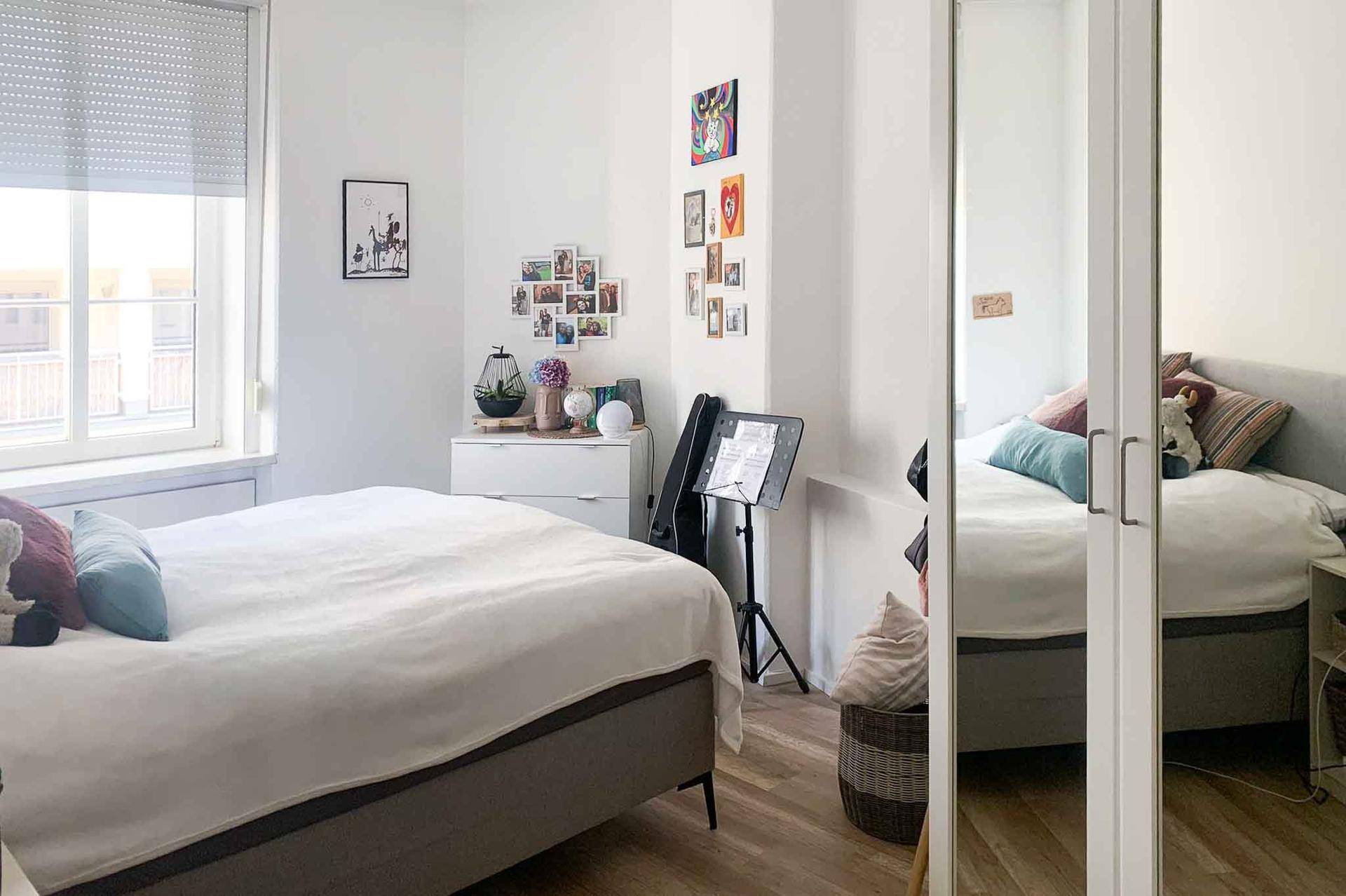 Helles Schlafzimmer mit Doppelbett, Spiegelschrank und farbenfroher Wanddekoration.