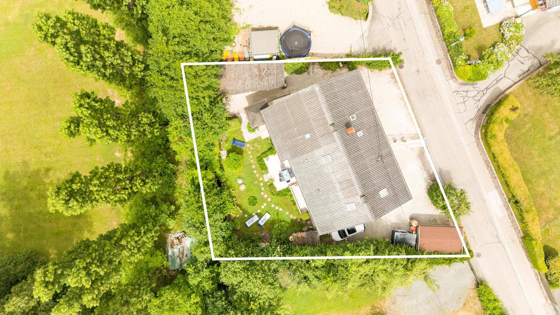 Luftaufnahme eines Hauses mit Garten, umgeben von Bäumen und einer Straße, Grundstücksgrenze markiert.