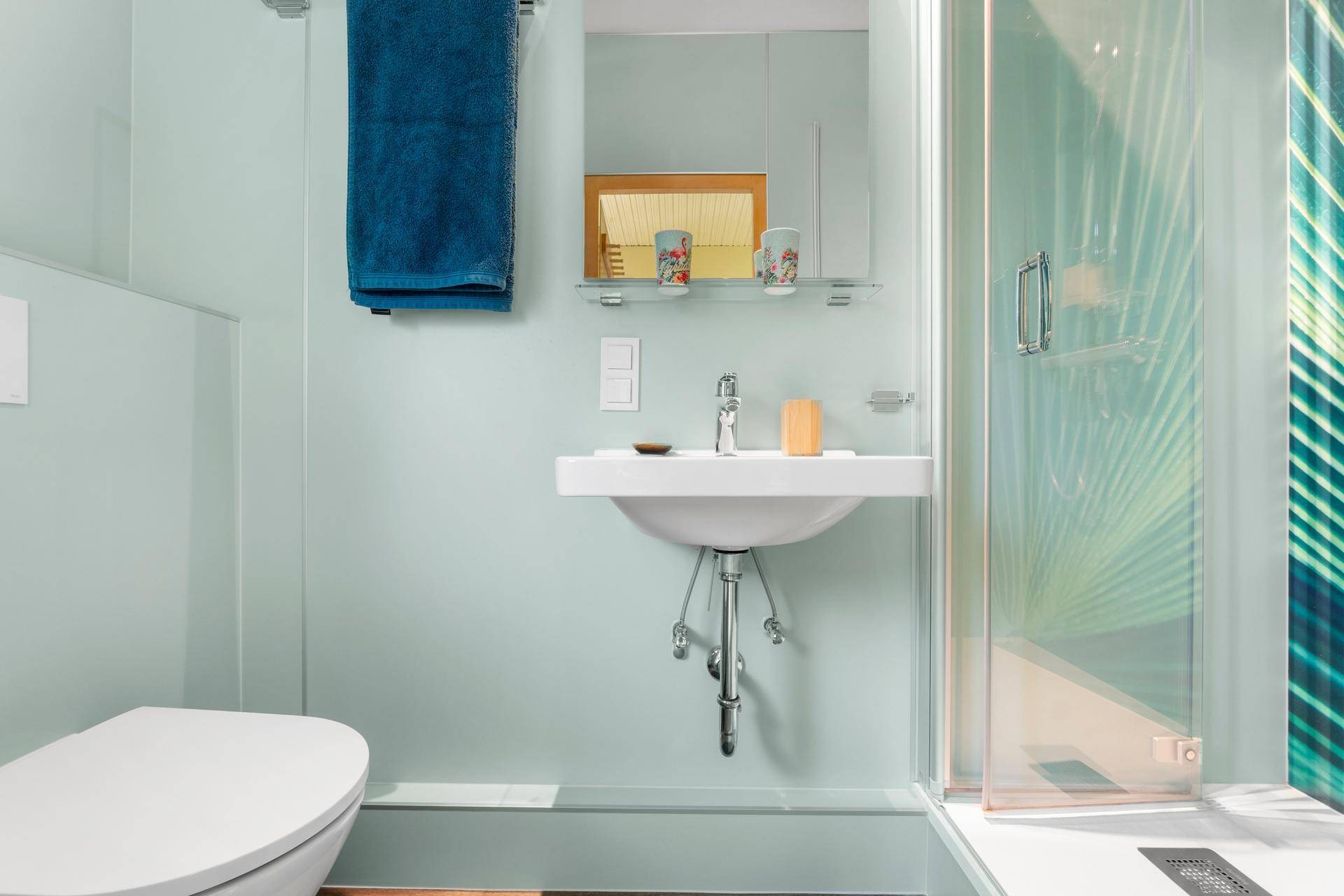 Kompaktes Badezimmer mit Dusche, WC und Waschbecken, in hellblauen Farbtönen gehalten.