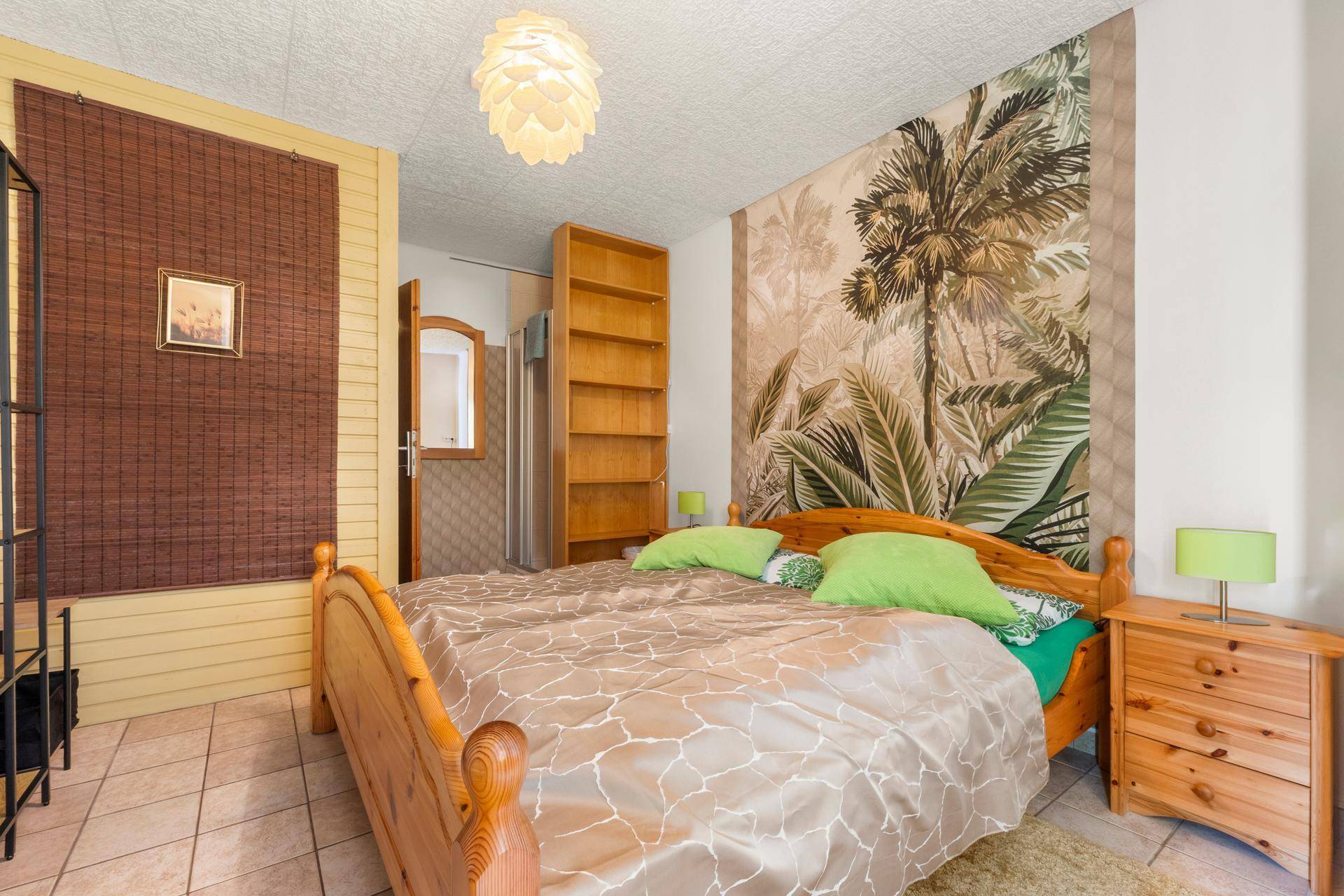 Gemütliches Schlafzimmer mit Holzbett, tropischer Tapete und Duschbereich im Hintergrund.