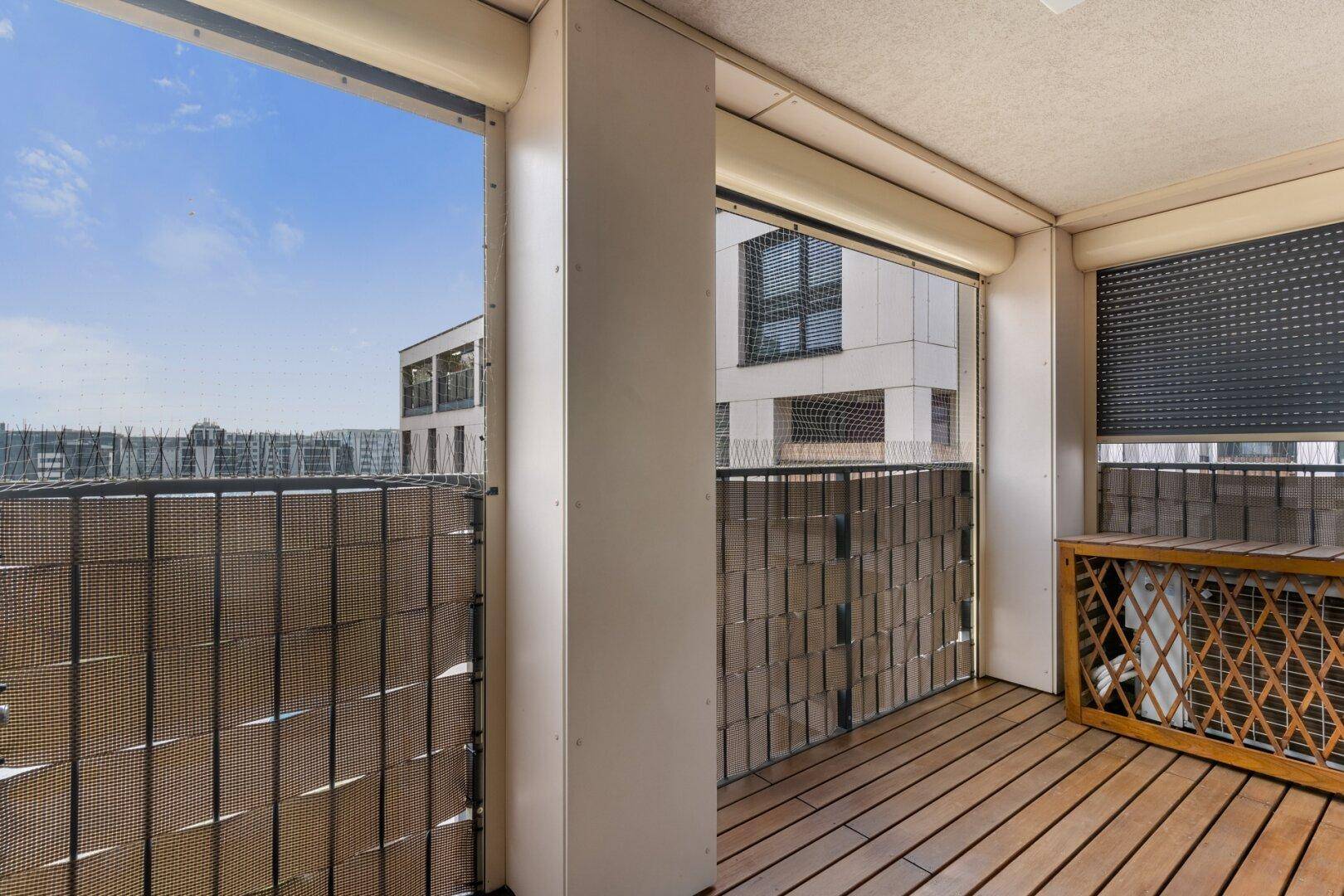 Gemütlicher Balkon mit Holzfußboden und Sichtschutz, bietet einen Blick auf die umliegenden Gebäude.