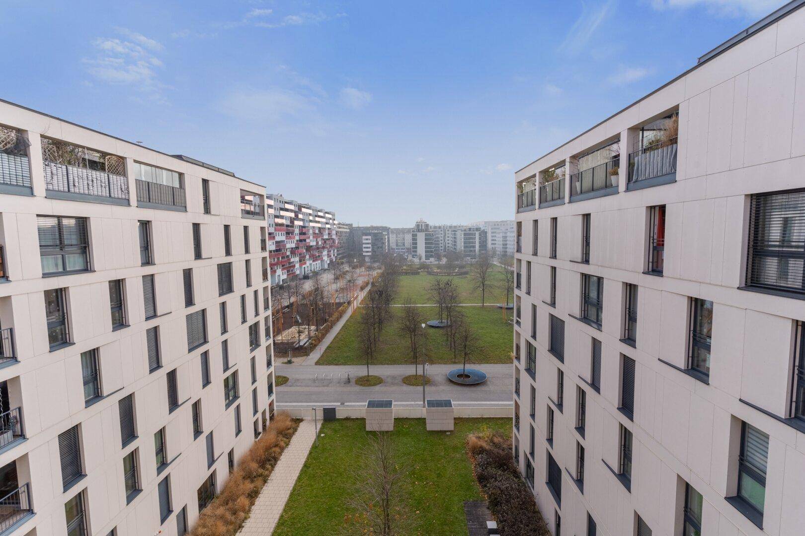 Weitläufiger Blick auf moderne Wohngebäude und eine grüne Parkanlage unter blauem Himmel.