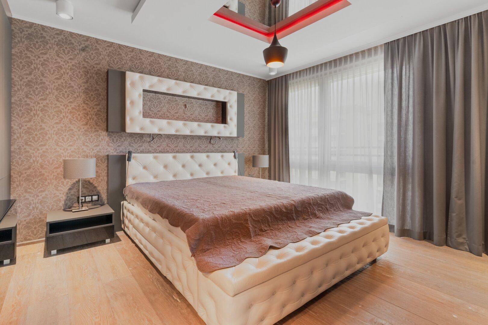 Elegantes Schlafzimmer mit großem Polsterbett, gemusterter Tapete und bodentiefen Vorhängen.